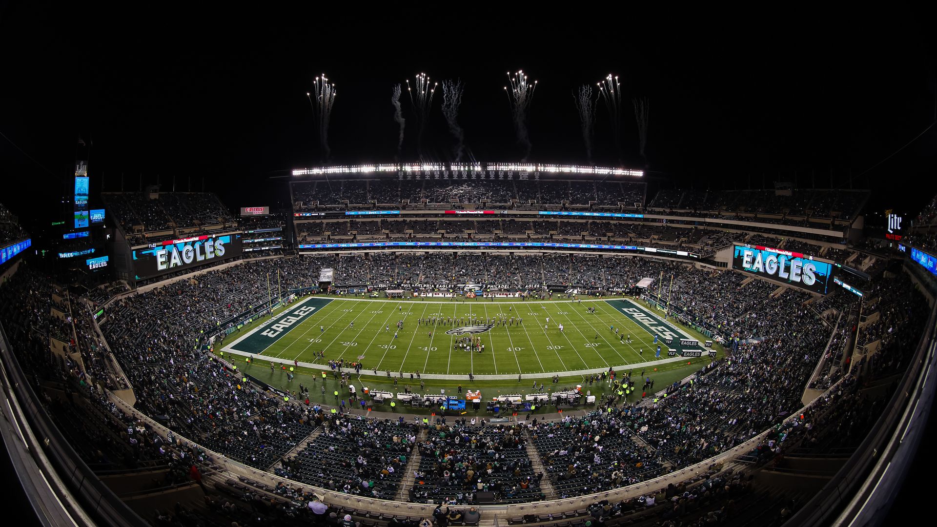 A football stadium at night filled with fans, the words "Eagles" written on two screens, fireworks firing in the air. 