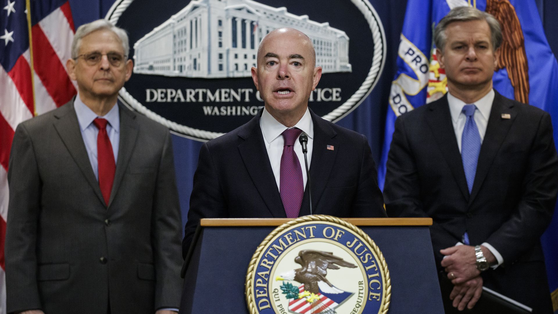 Mayorkas speaks at a podium surrounded by Wray and Garland 