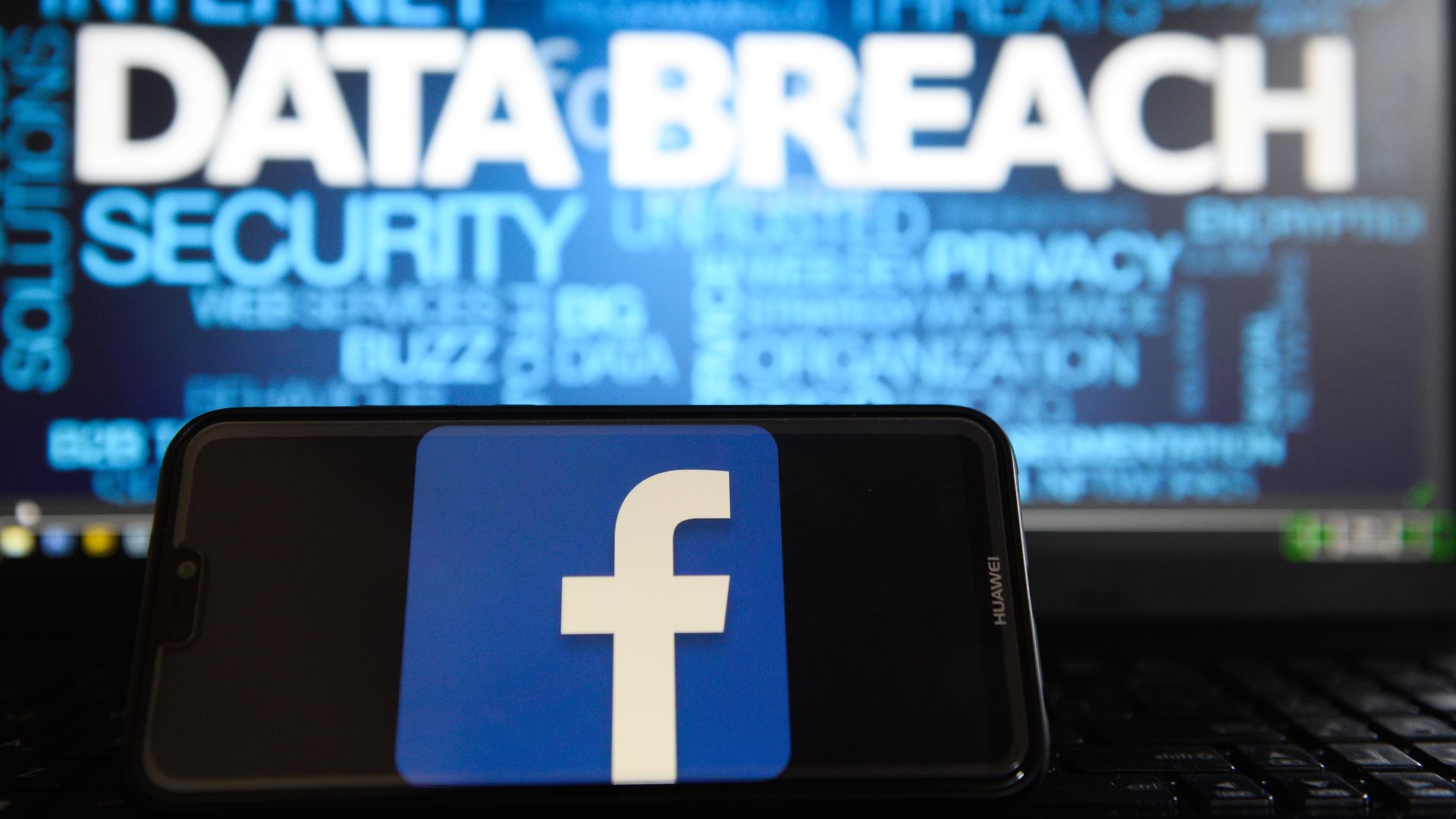 Facebook logo is seen on a Huawei smart phone with the word "data breach" on a laptop monitor.