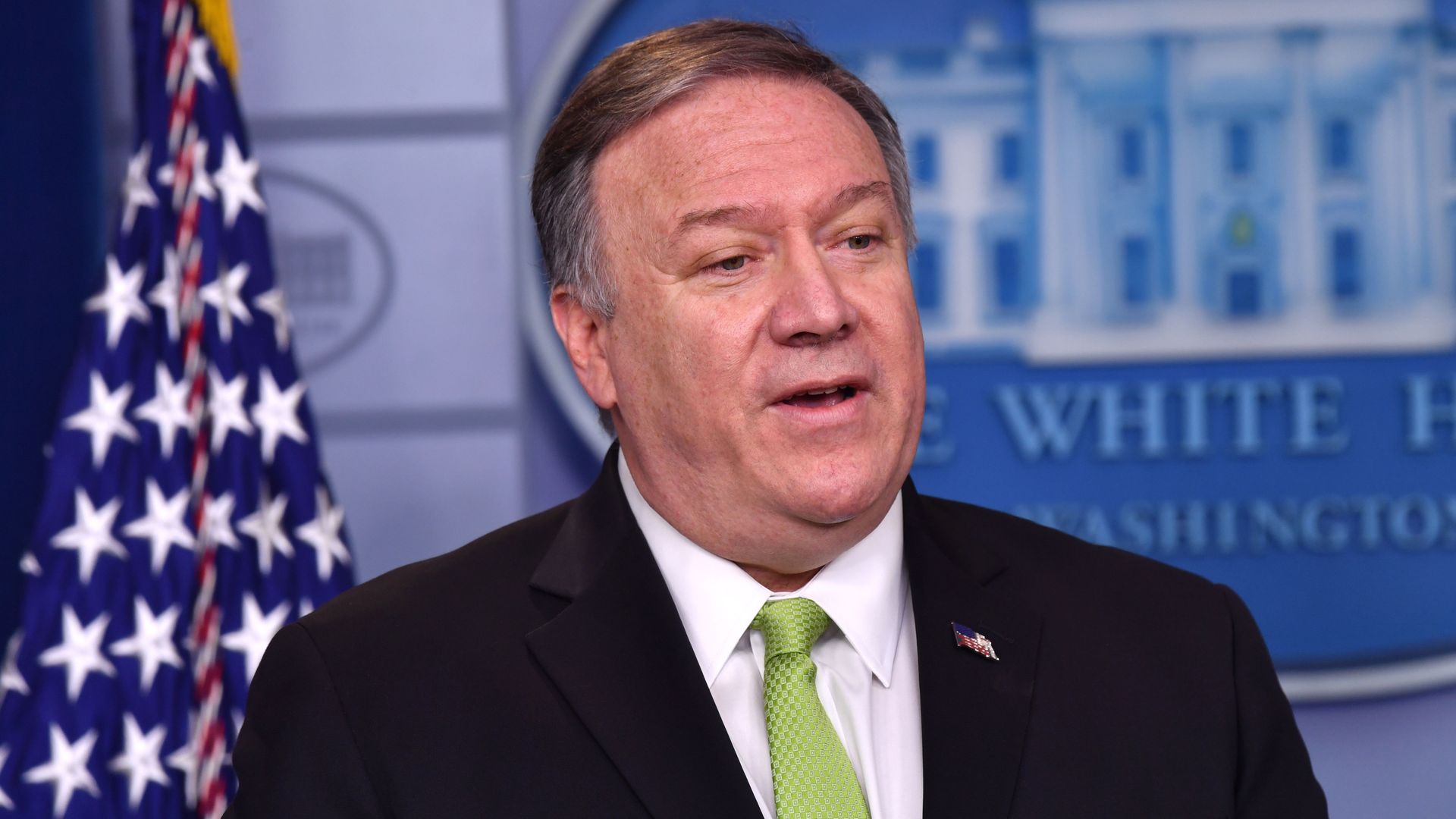 In this image, Mike Pompeo stands in front of a White House logo