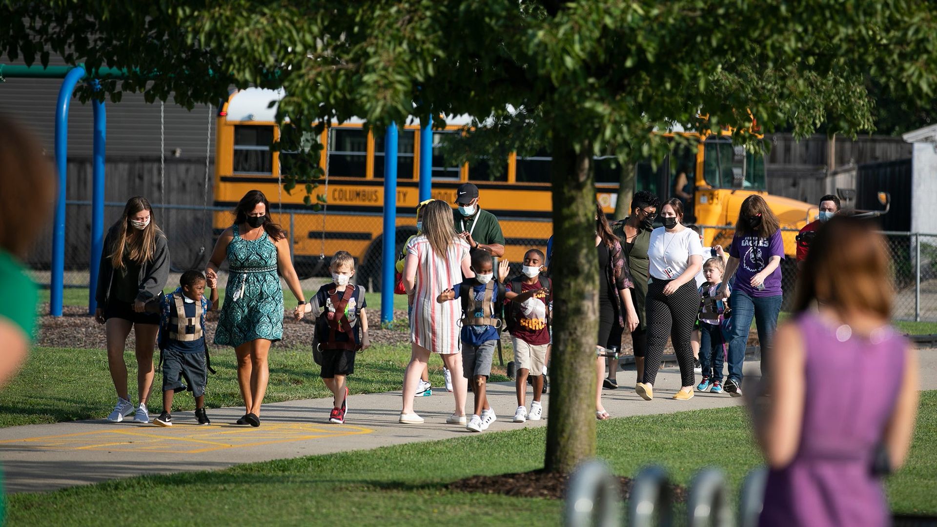 Teachers walk students from a school bus to the building.
