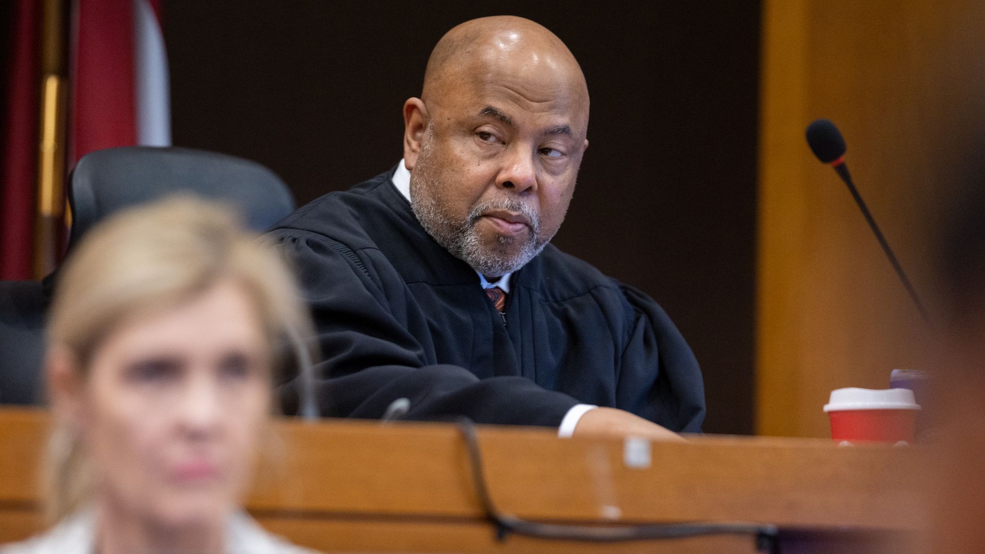 A judge sitting at the dais looks to their right while a court reporter works in the foreground