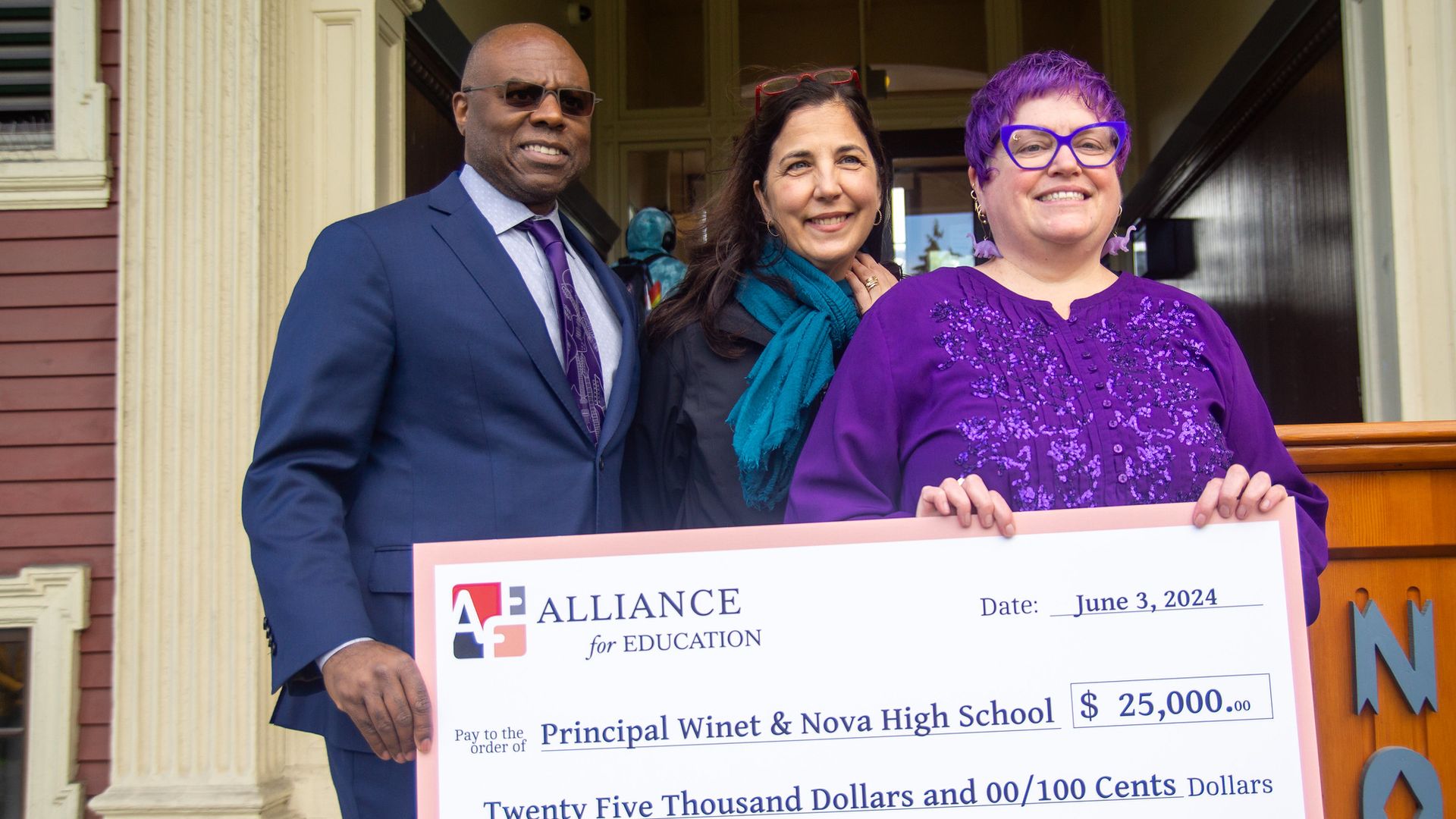Three people stand smiling with a large ceremonial check for $25,000 awarded to Principal Winet and Nova High School from the Alliance for Education.