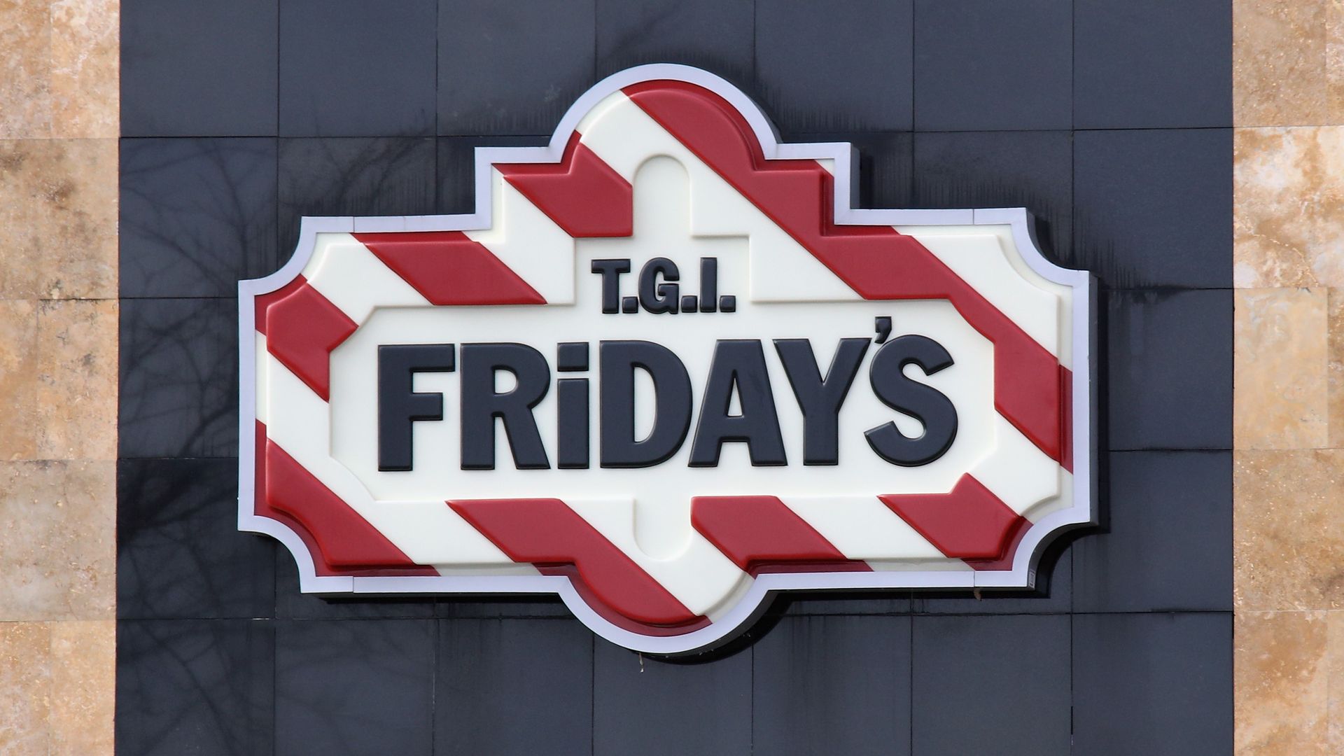 TGI Friday's sign with red and white diagonal striped border, on a black stone wall background. 