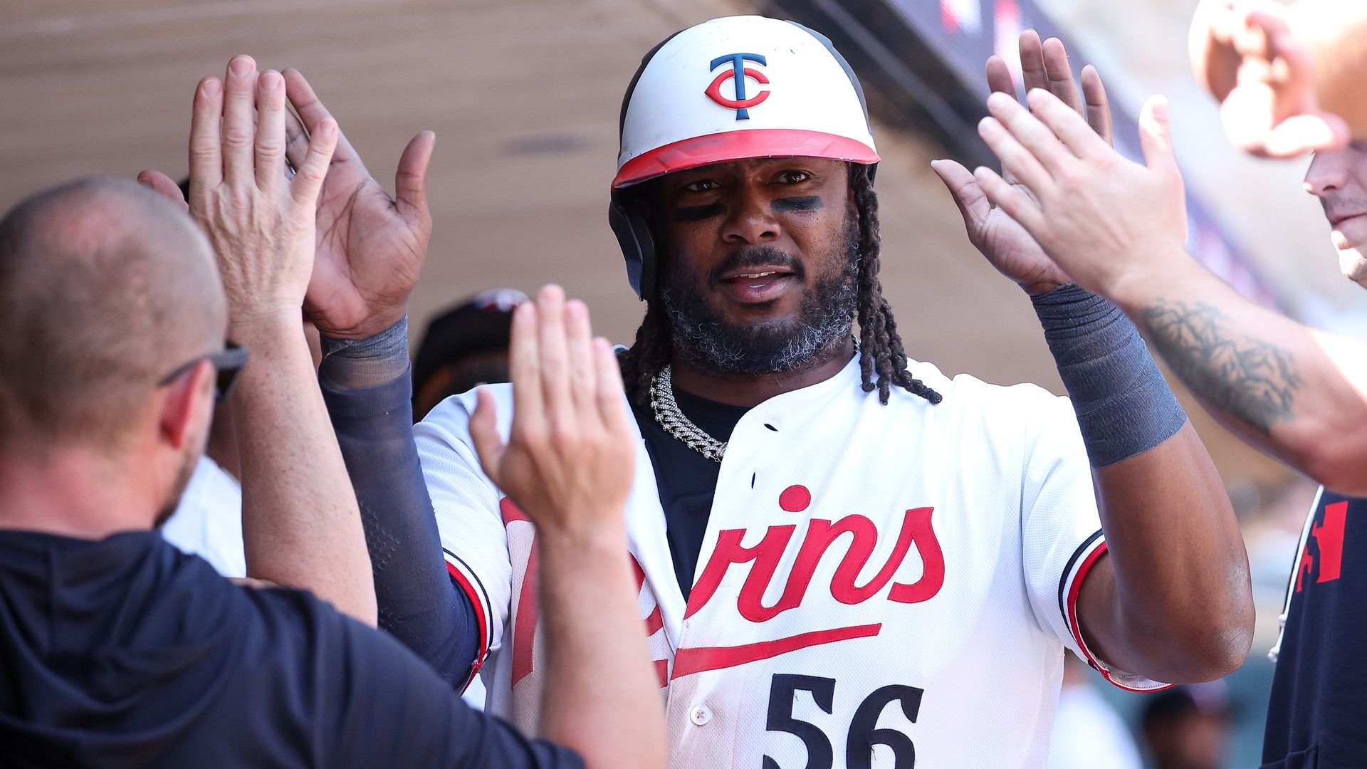Baseball player wearing a white Minnesota Twins jersey and helmet with a red brim, black eye paint, and braids, high-fiving fans on both sides during a celebration.