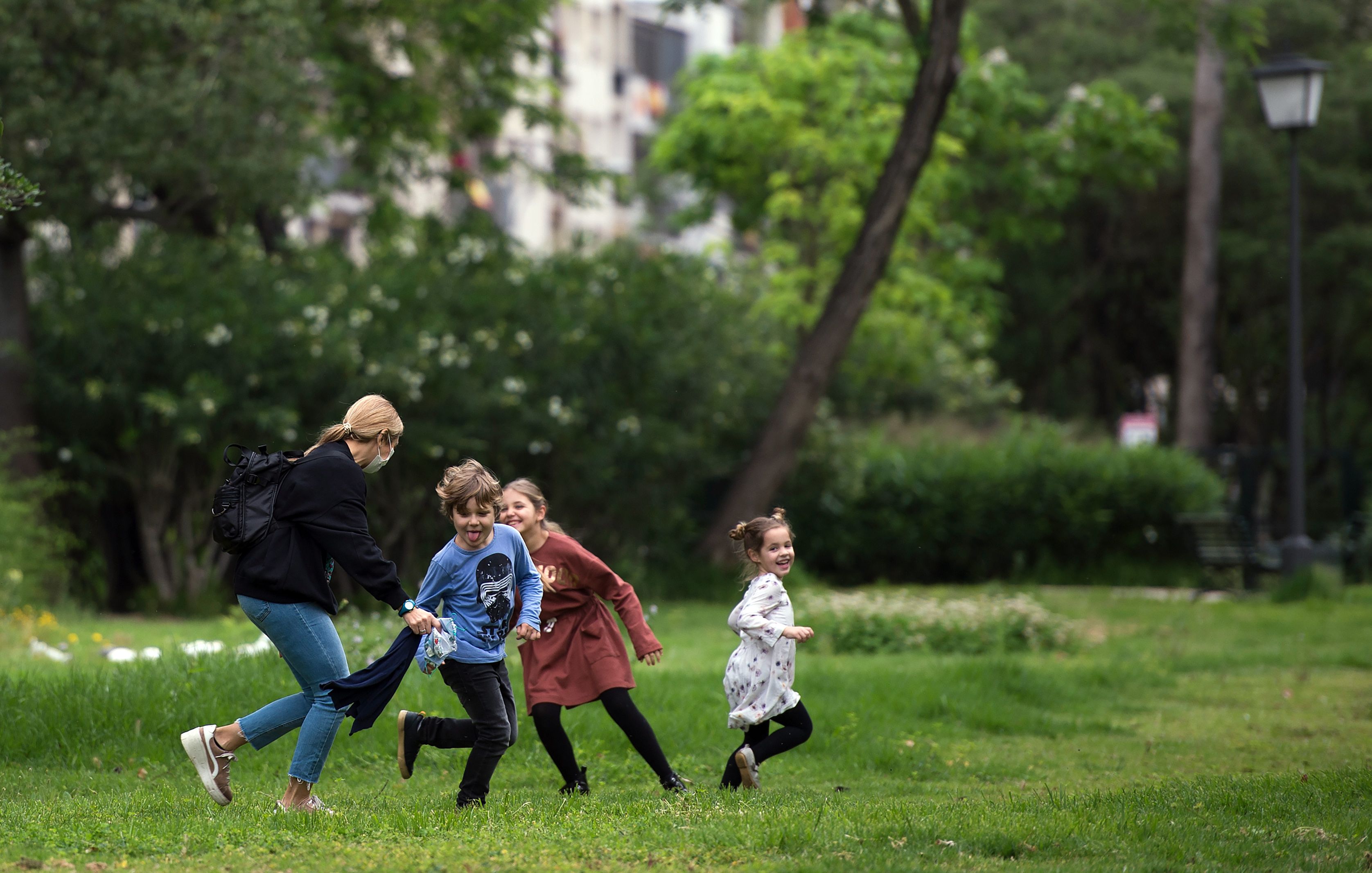 In this image, a woman plays tag with kids in a park
