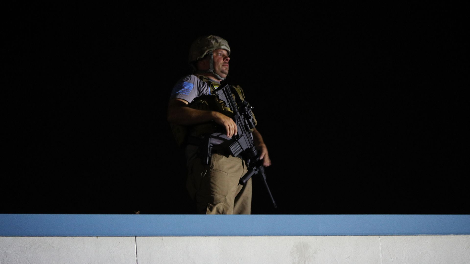 A man stands in the night in a helmet holding a rifle