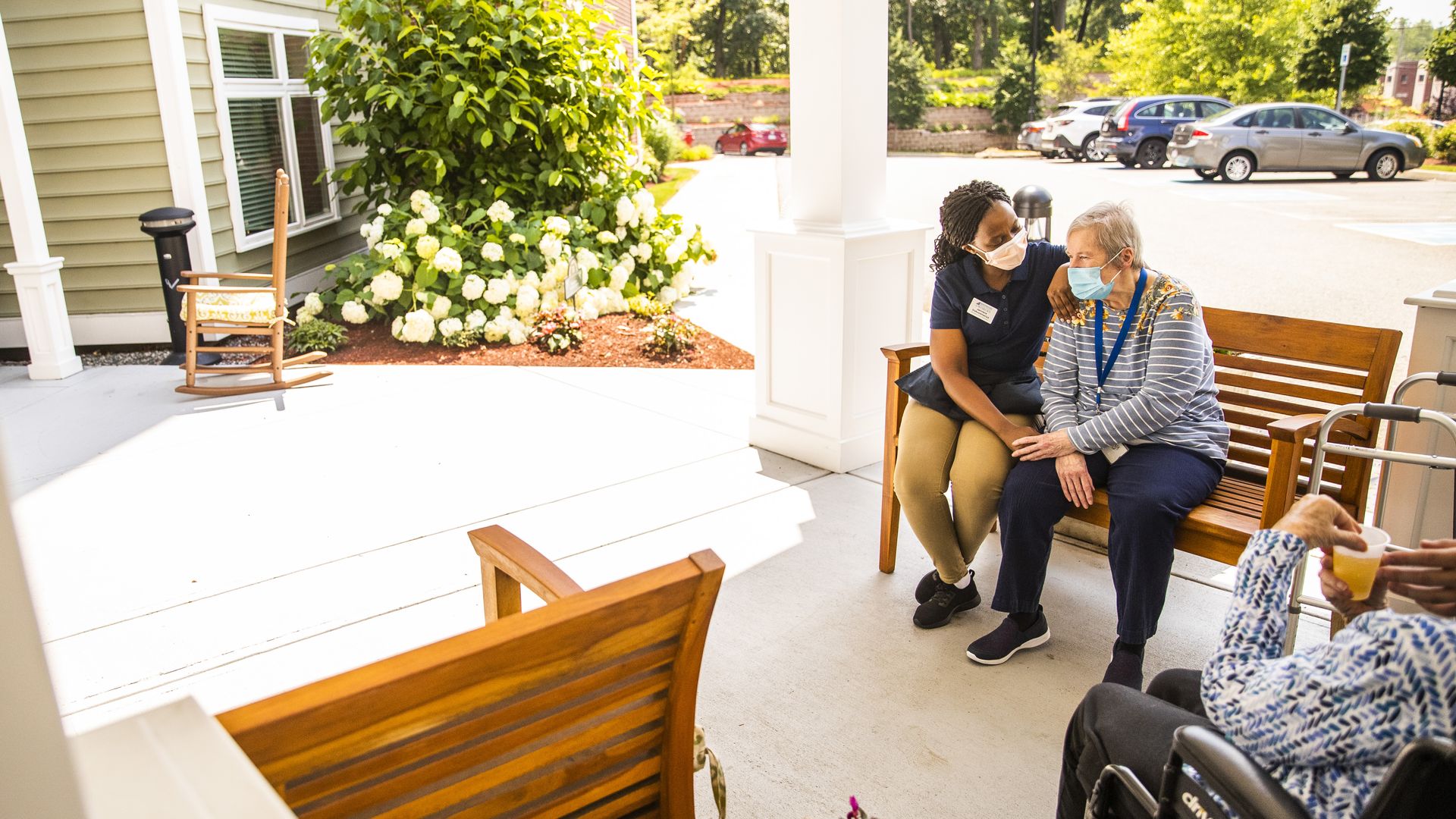 Photo of a nursing home worker sitting beside a senior resident on a bench located on a front porch