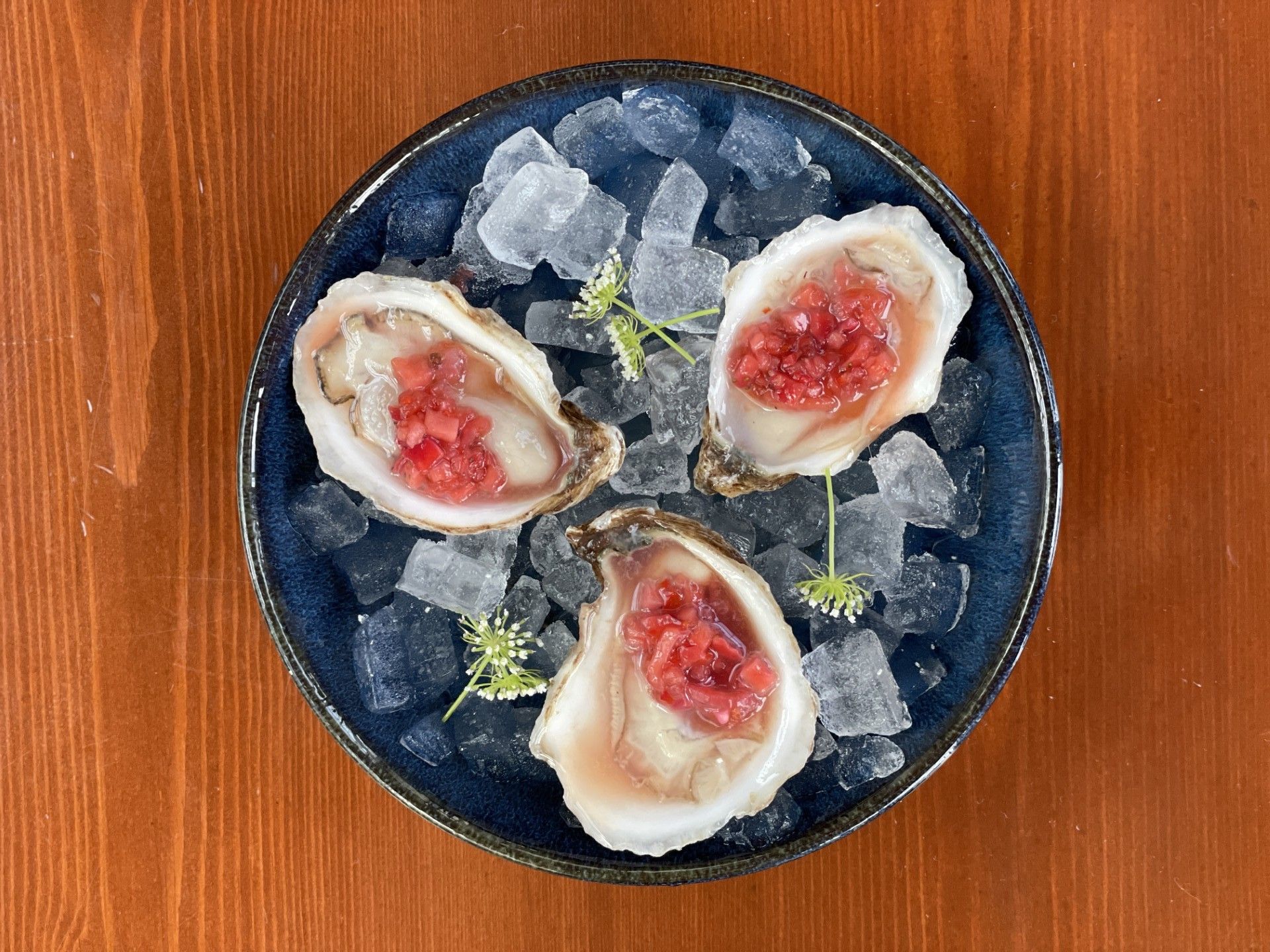 Three oysters with red jam on top of ice in a bowl.