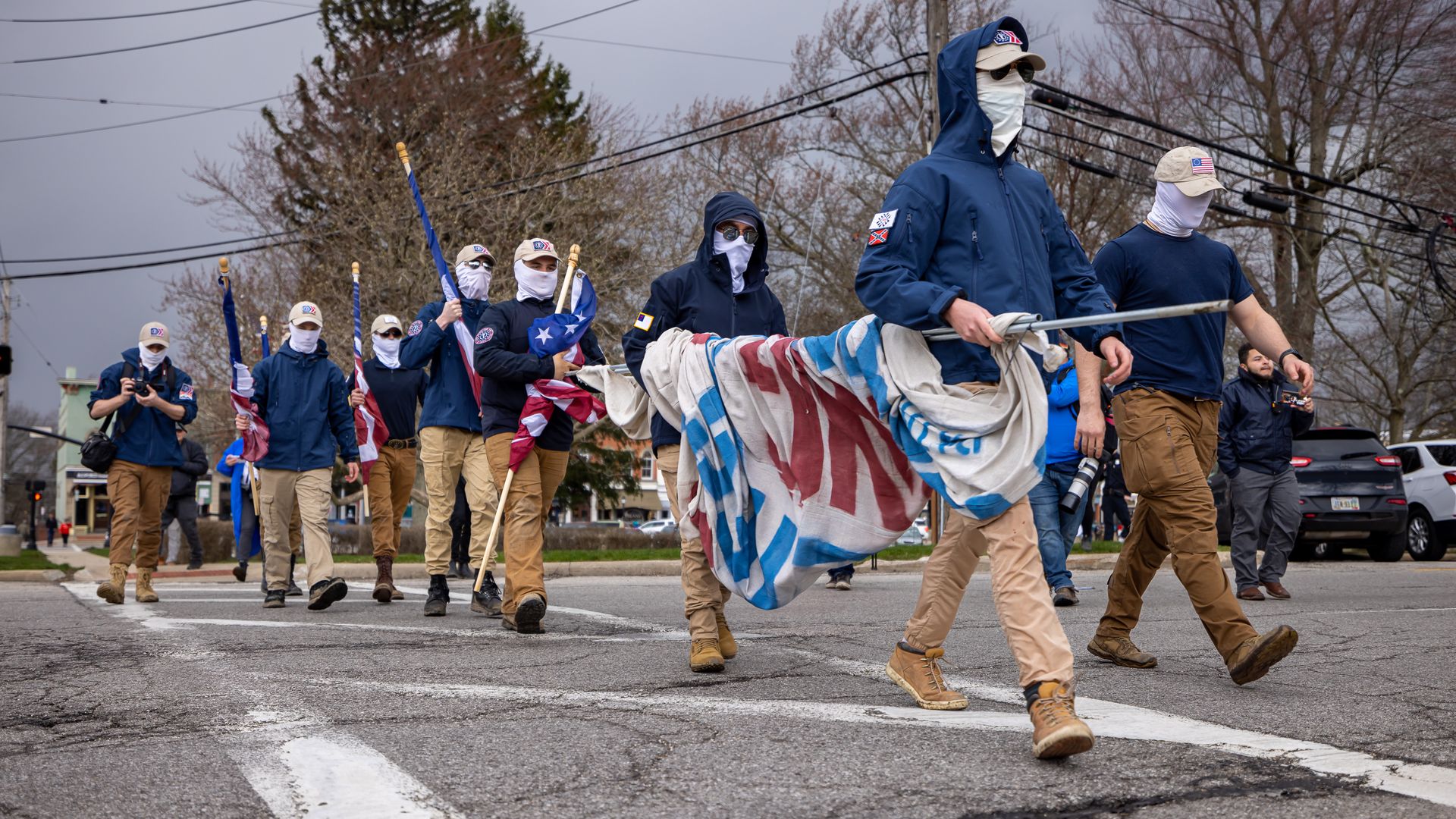Members of a white supremacist group march down the street in masks and holding flags. 