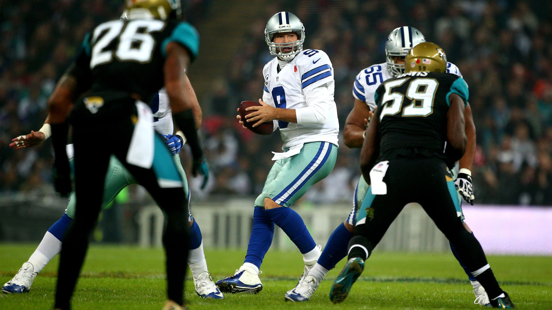 Tony Romo holds the ball on a field, surrounded by Jaguars players