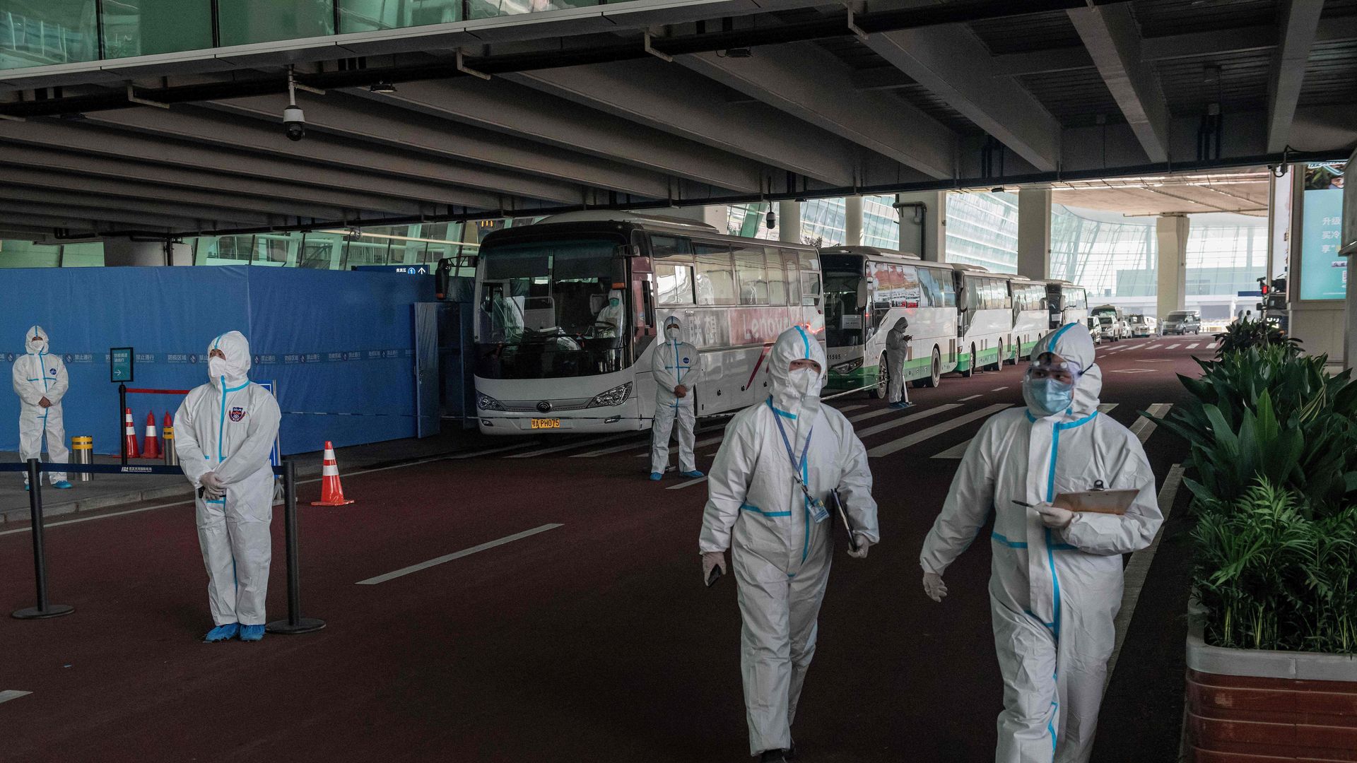 Health workers in personal protection suits stand next to buses at a cordoned-off section at the international arrivals area, where arriving travellers are to be taken into quarantine in Wuhan