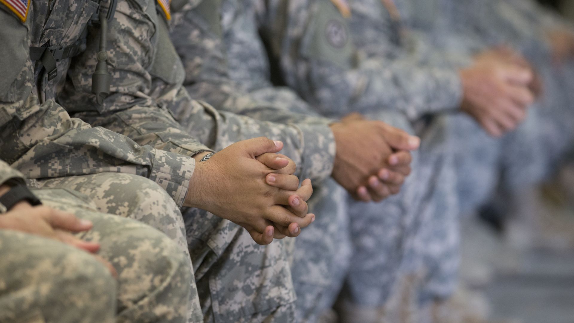 National Guard troops' hands clasped together as they sit in a row in uniform.