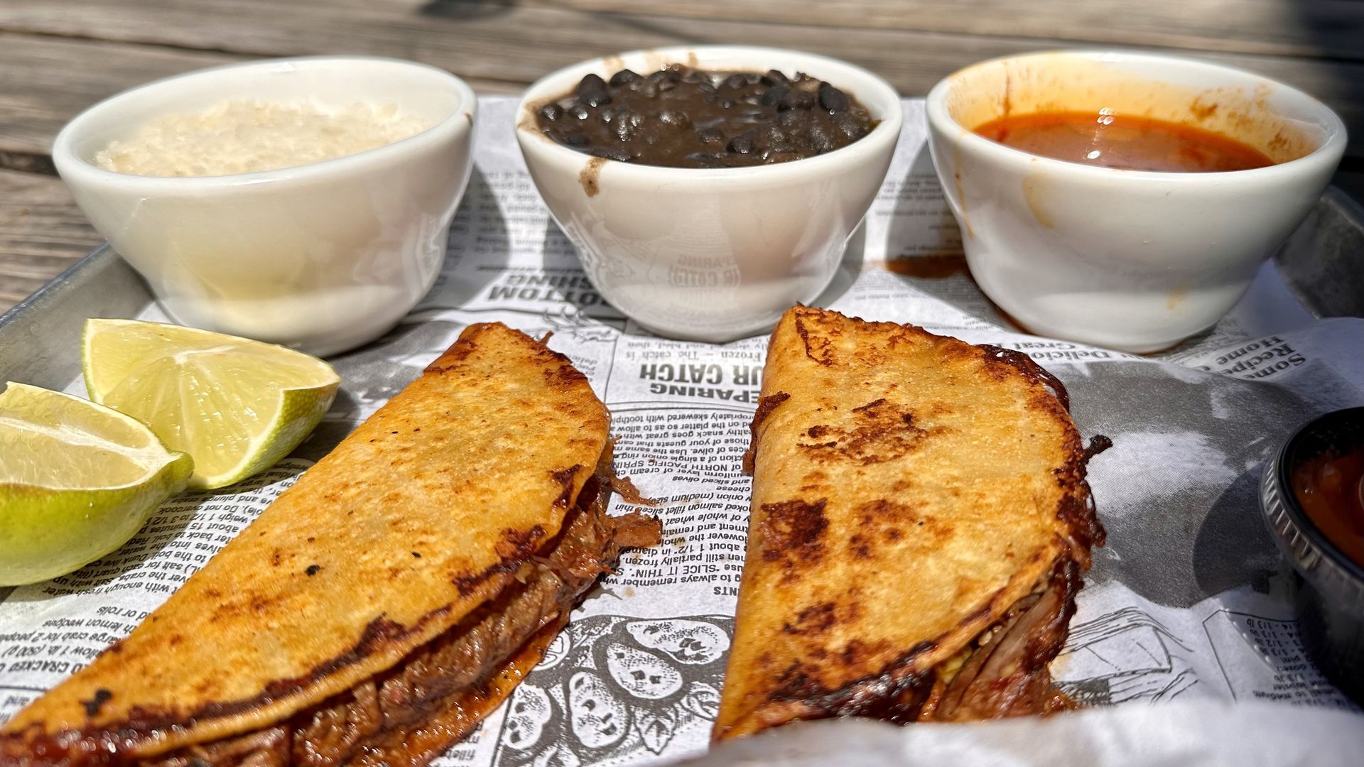 A photo of birria tacos and cups of rice, beans and broth