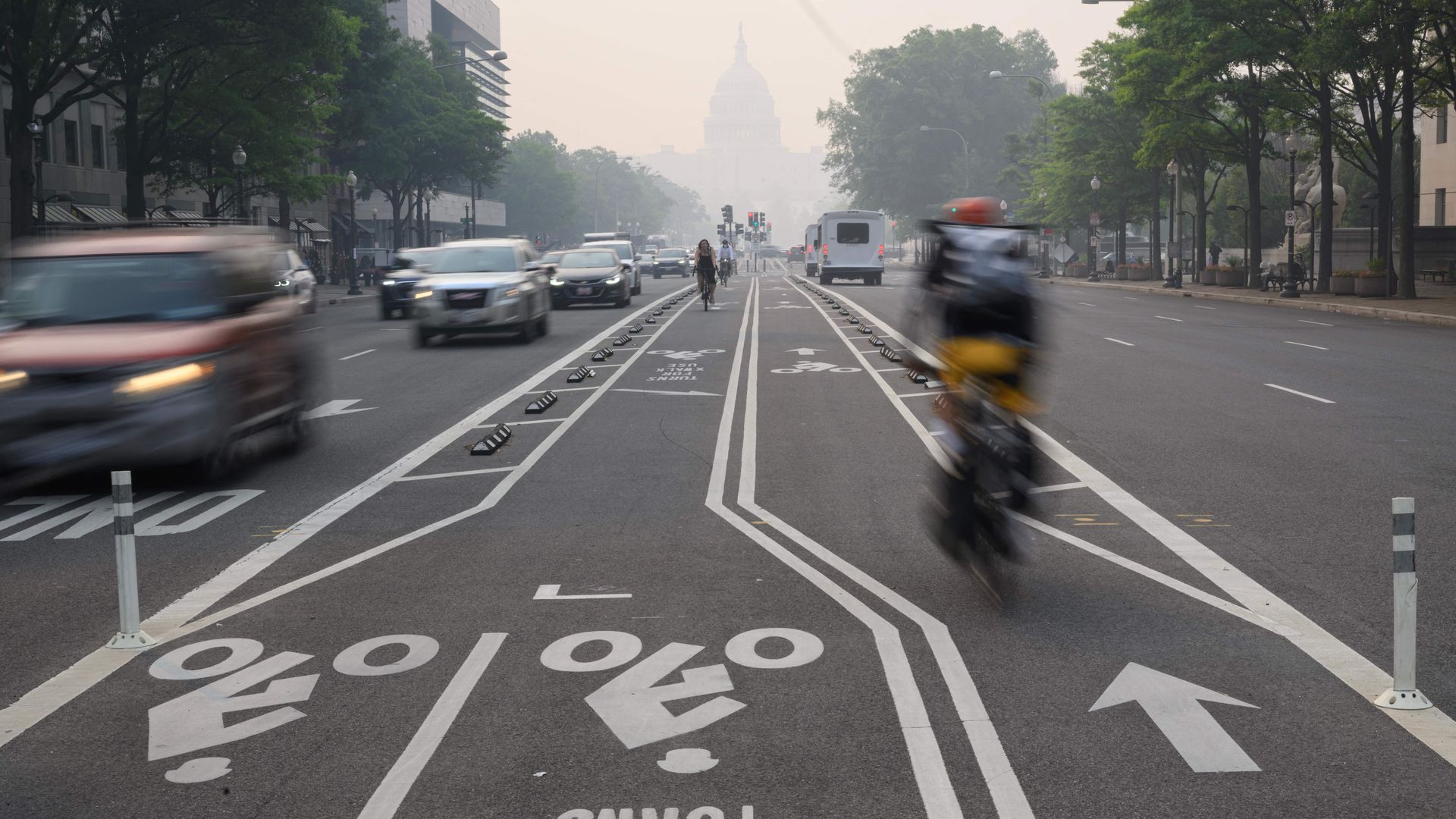 A person rides a bicycle on Pennsylvania Avenue with haze in the background obscuring the U.S. Capitol building