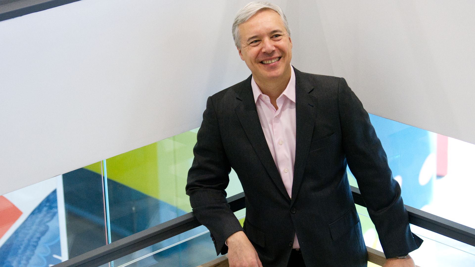 Horacio, a man in a black suit and white-ish shirt, stands in a stairwell. He is leaning against the bannister and smiling.