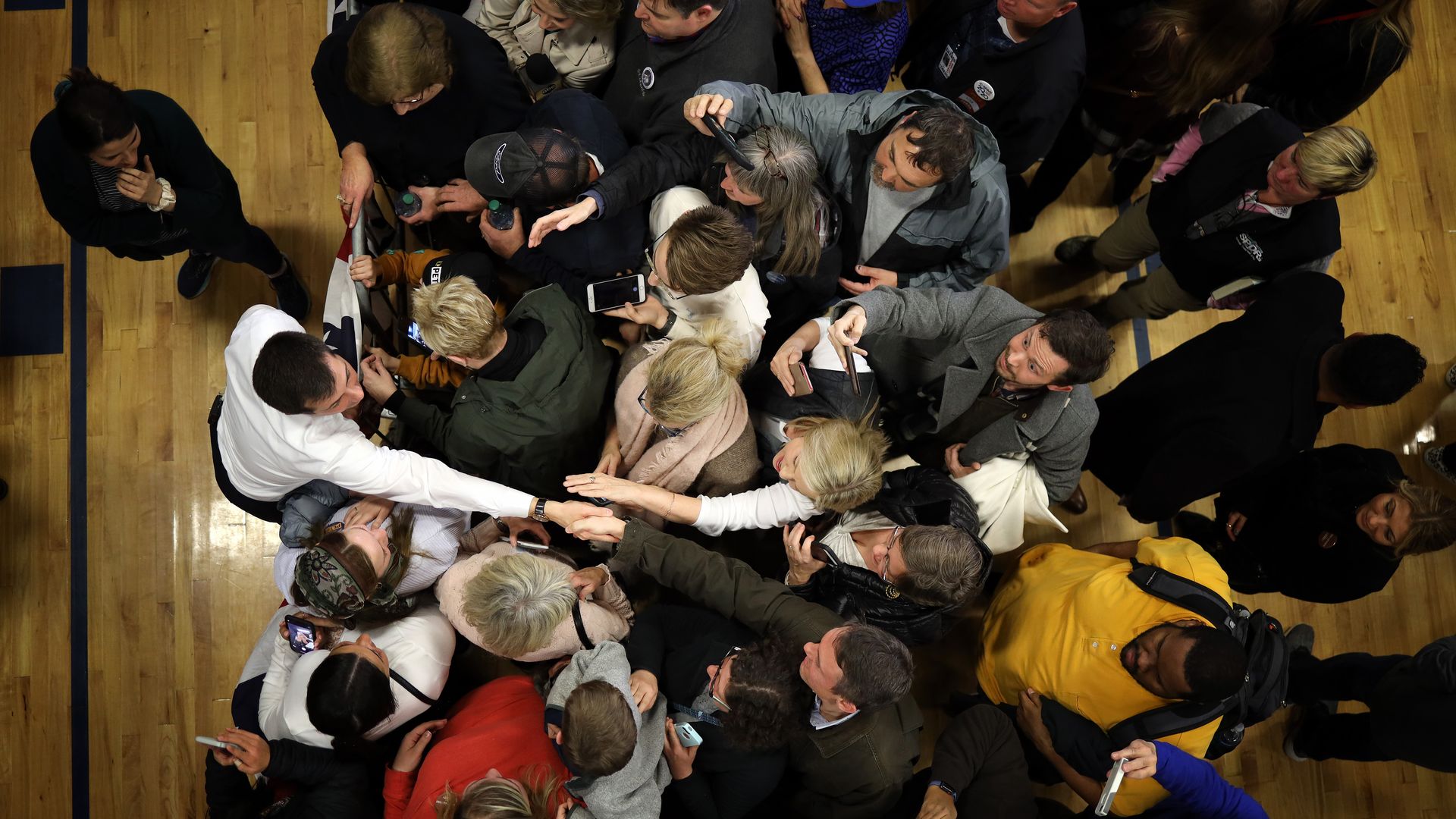 In this image, Pete Buttigieg wears a white dress shirt and reaches for a crowd of supporters