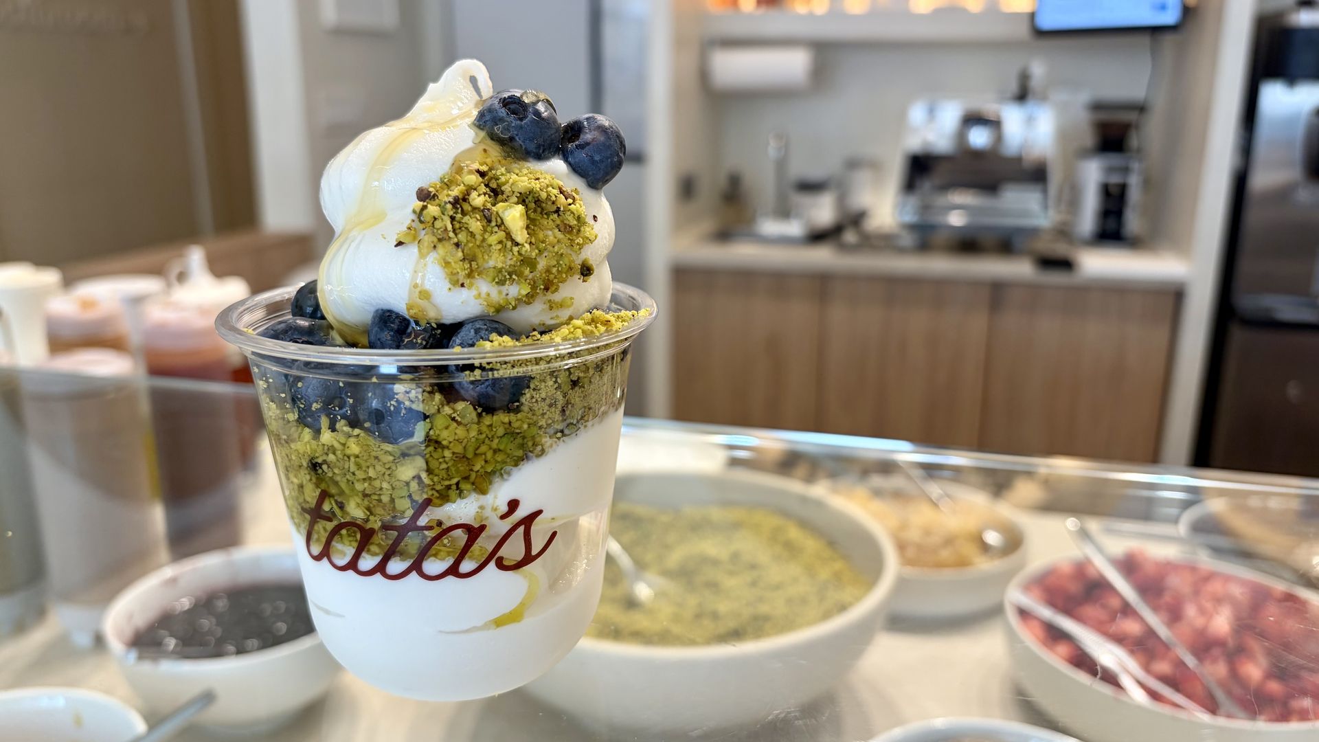 Dessert parfait in a clear cup, layered with yogurt, blueberries and pistachio crumbs.