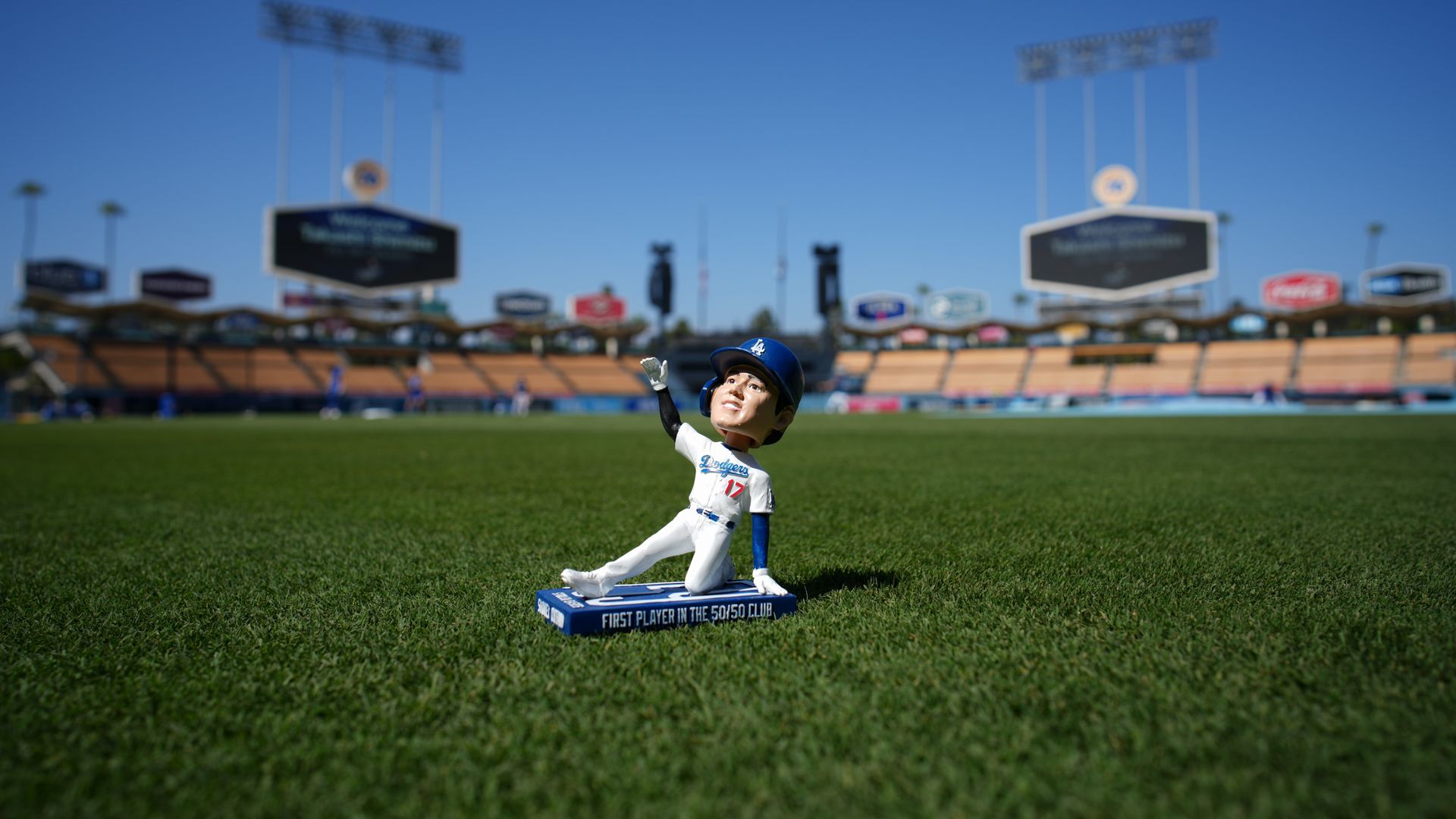 A bobblehead figurine of a Los Angeles Dodgers player wearing a blue helmet, white uniform with number 17, kneeling and pointing up, on the grass of a baseball stadium field.