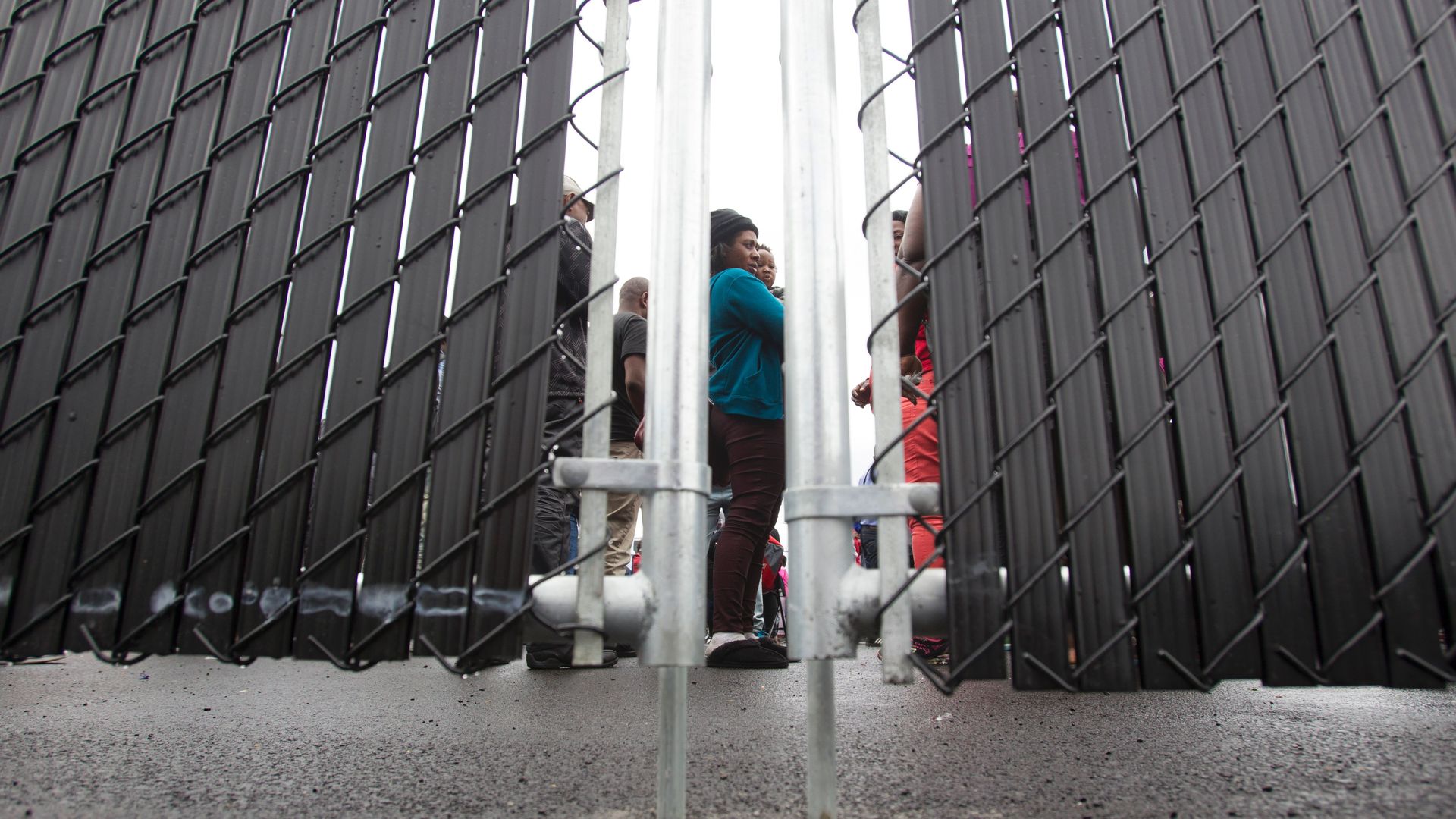 Refugees who crossed the Canada/US border illegally stand behind a fence.