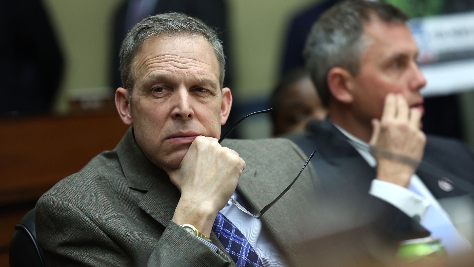 Photo of Scott Perry holding his glasses in his hand as he looks to his right