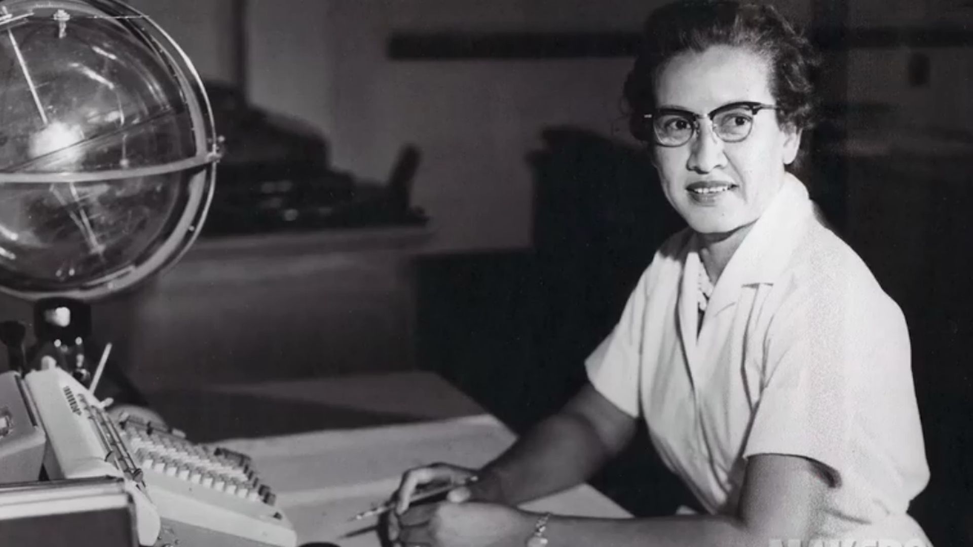 Katherine Johnson at a desk with a globe sitting on it at NASA in black and white