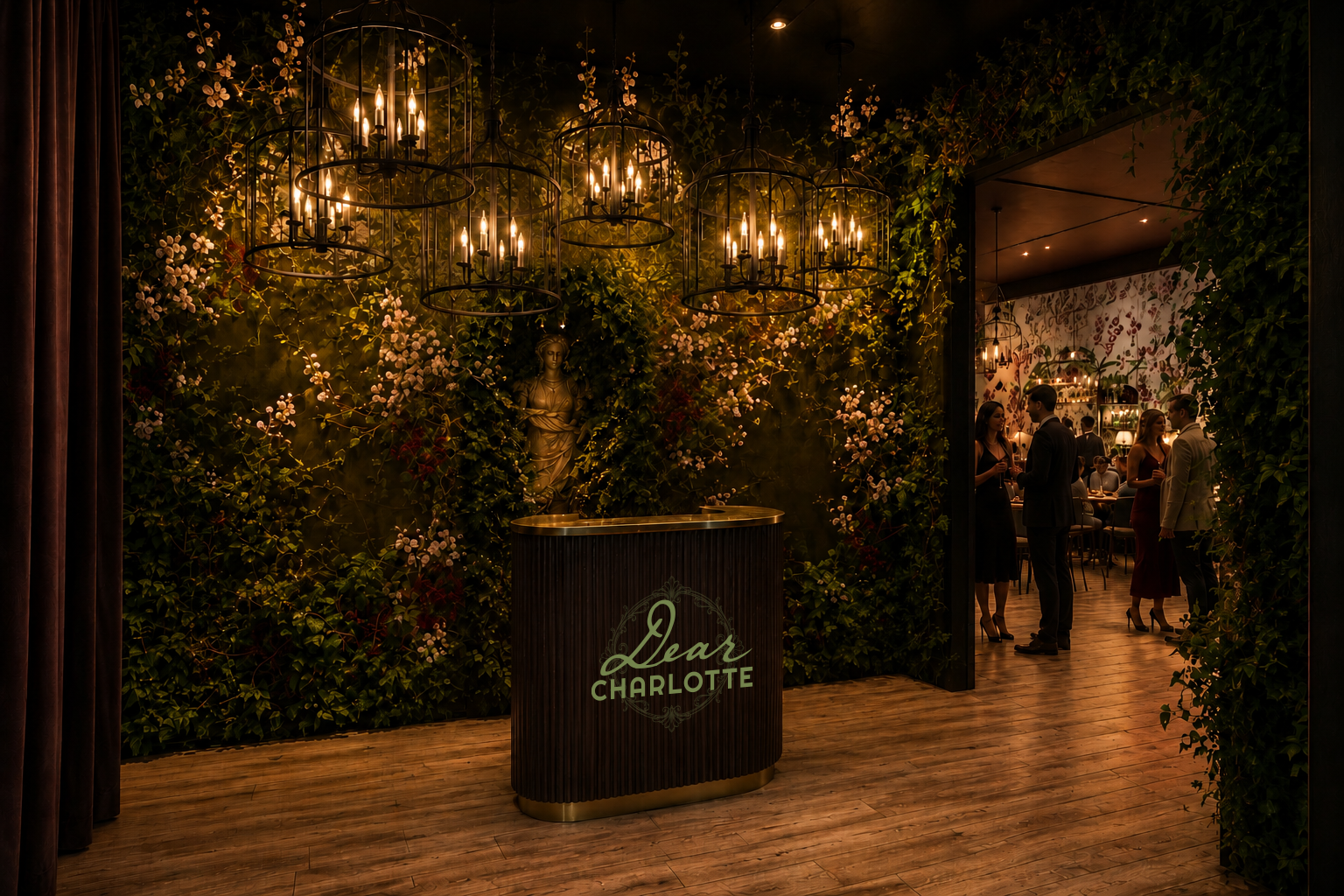 Dimly lit lounge with a curved dark wood reception desk reading "Dear Charlotte" in mint. A statue stands against a lush green floral wall; warm chandeliers glow as guests mingle beyond a doorway.