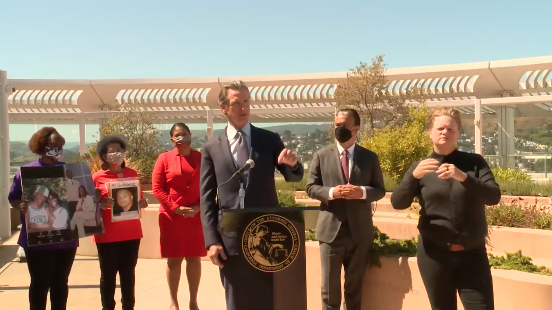 Photo of Gavin Newsom speaking from a podium with Rob Bonta and associates standing behind him in an open courtyard