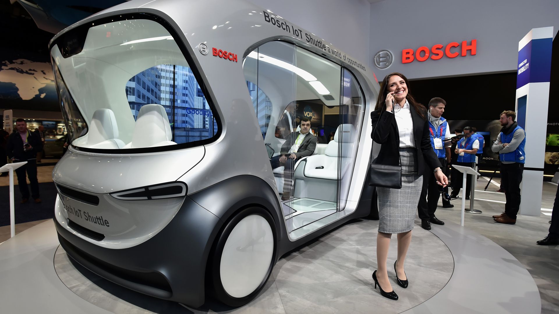 A woman stands near a Bosch automatous shuttle on display at CES