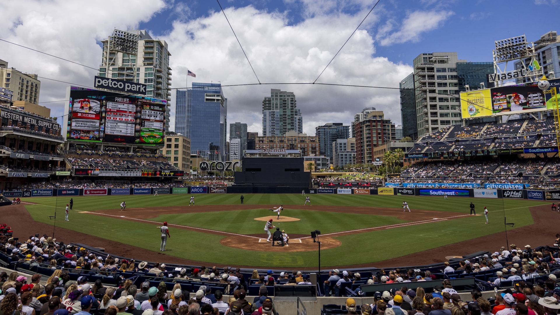 A view of Petco Park from behind home plate during a sunny afternoon game with fans in the stands.