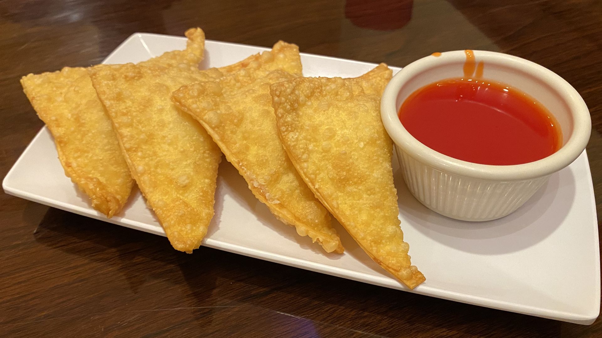 Four crab rangoons with a cup of sweet and sour sauce on a white rectangle plate