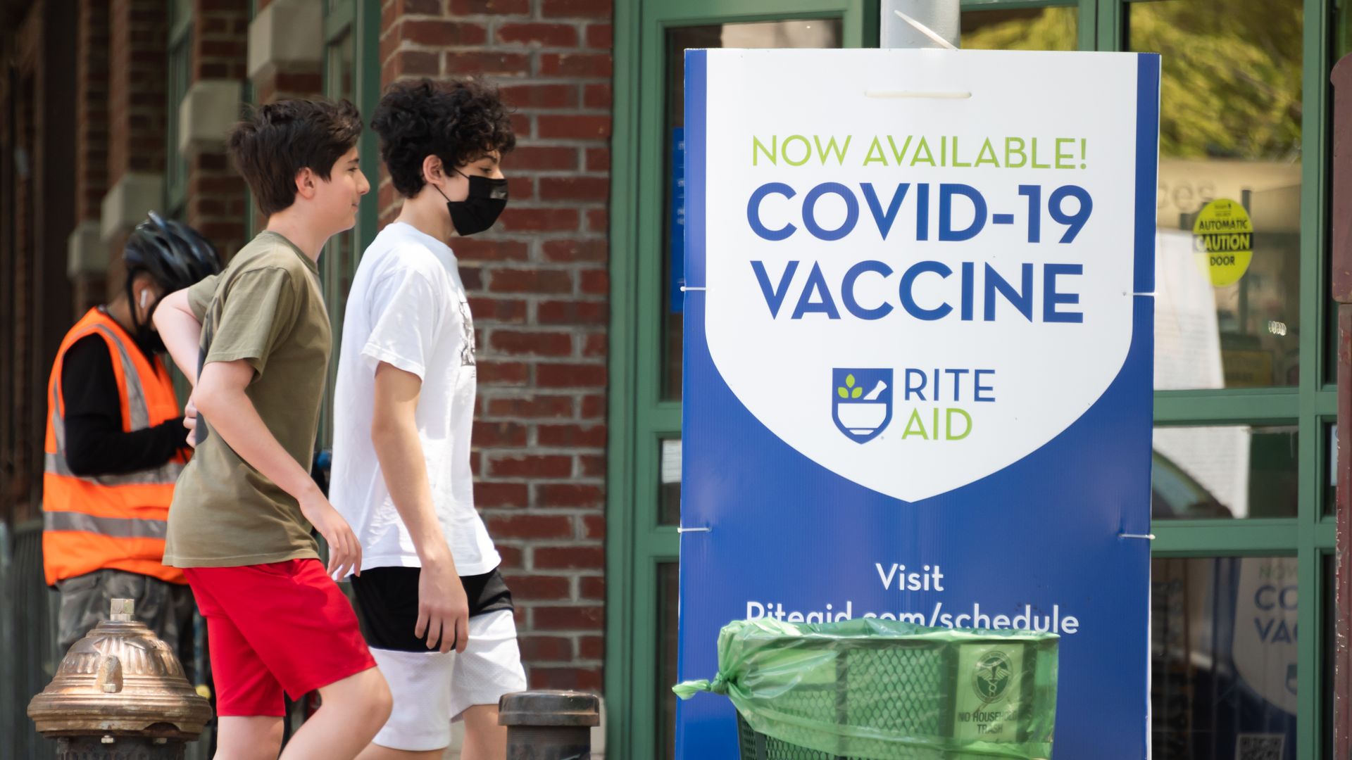 Photo of two adolescents walking by a sign that says "COVID-19 vaccine"