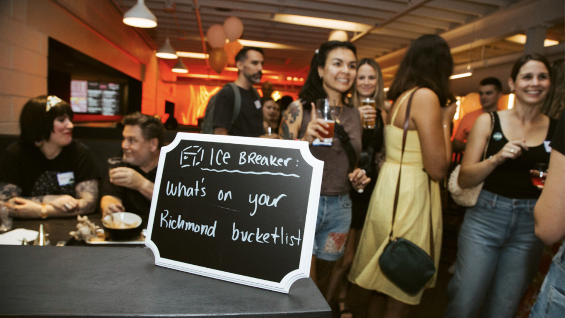 People congregating and smiling in the background. In front is a chalkboard that says "ice breaker what's on your richmond bucket list"