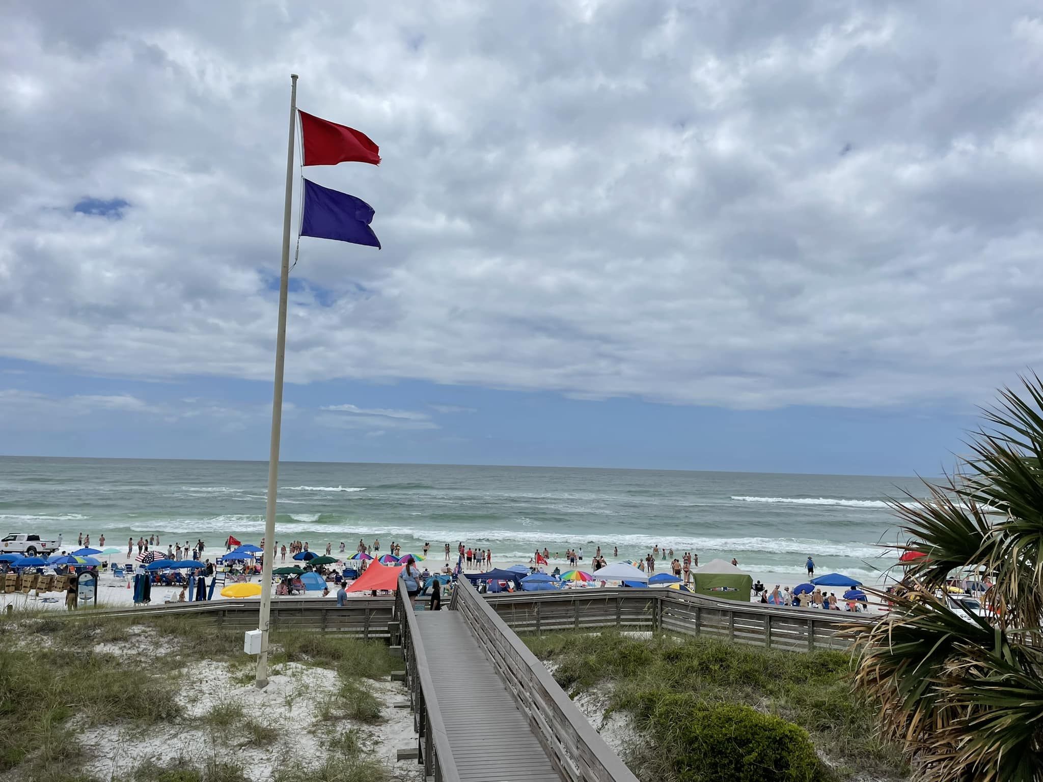 Photo shows a beach with a red and purple flag flying.