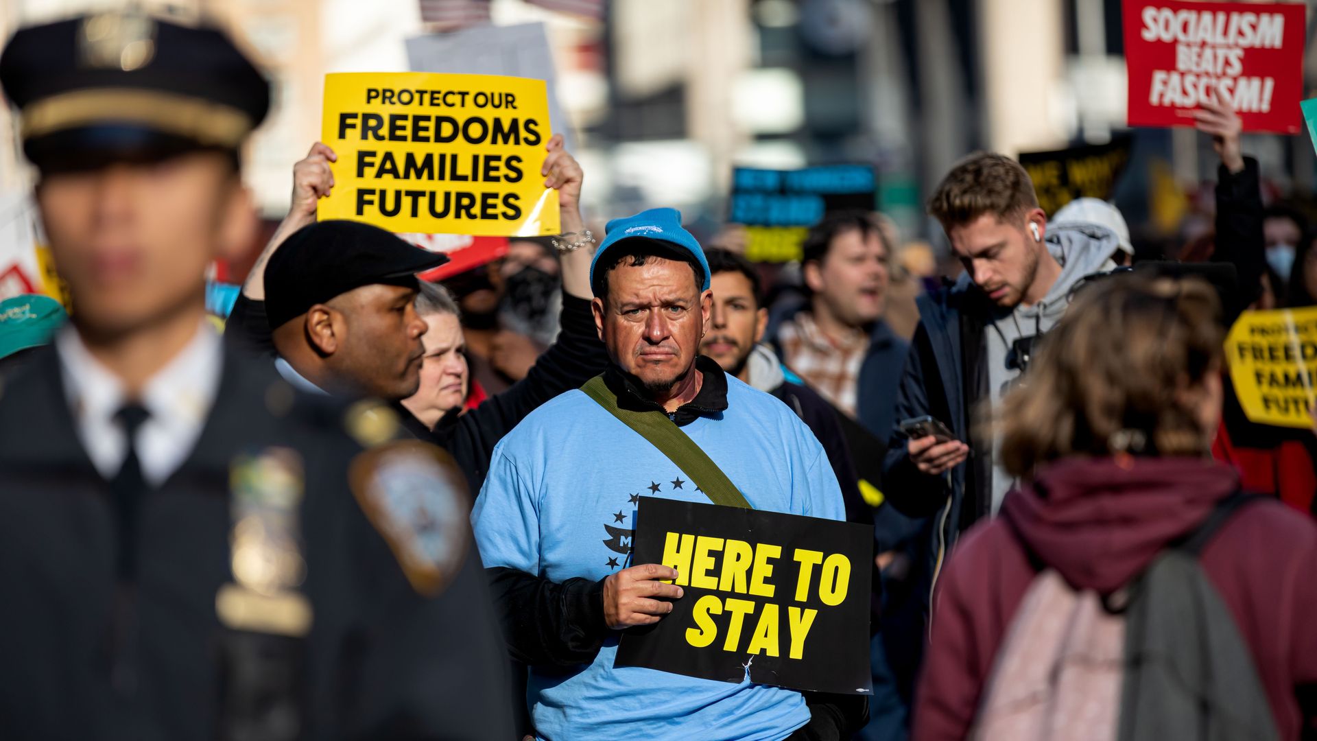 People hold protest signs reading "Protect our freedoms families futures," "here to stay," and "socialism beats facism."