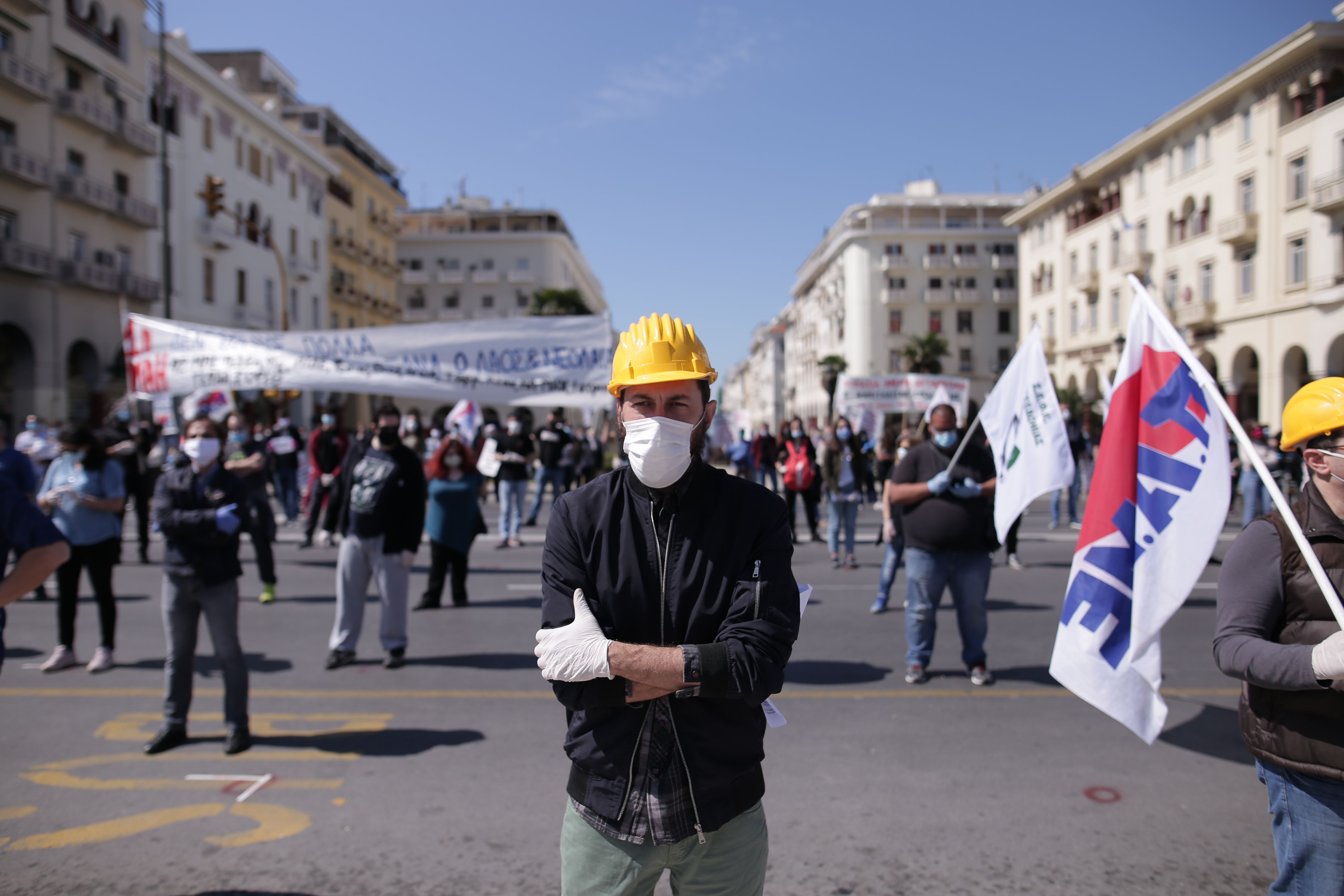 In this image, a man wearing a face mask and hard hats stands in the middle of a square during a protest