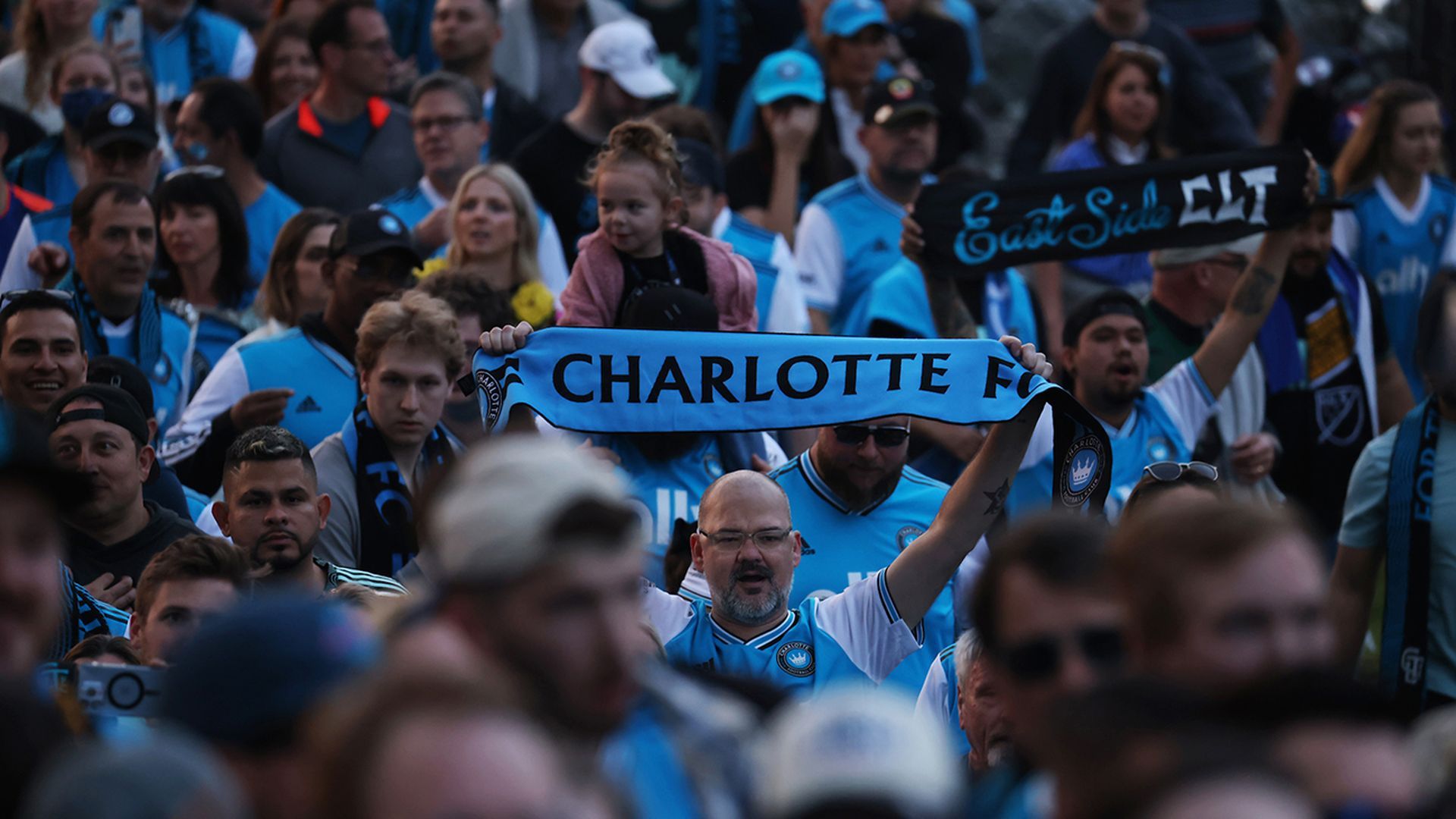 Charlotte FC supporters march to Bank of America Stadium with flags held high. 