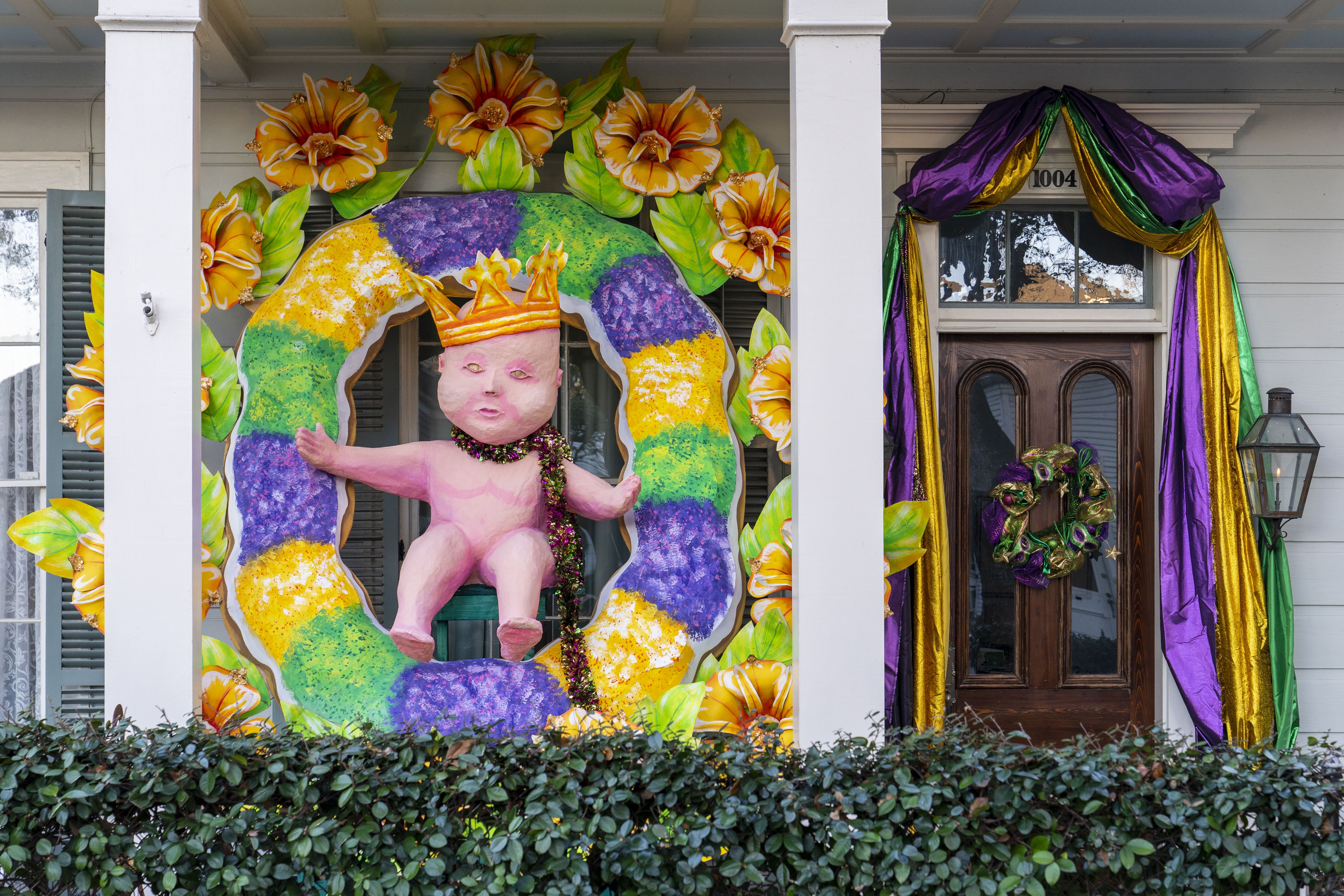 Photo shows a house float with a giant king cake and baby on the porch