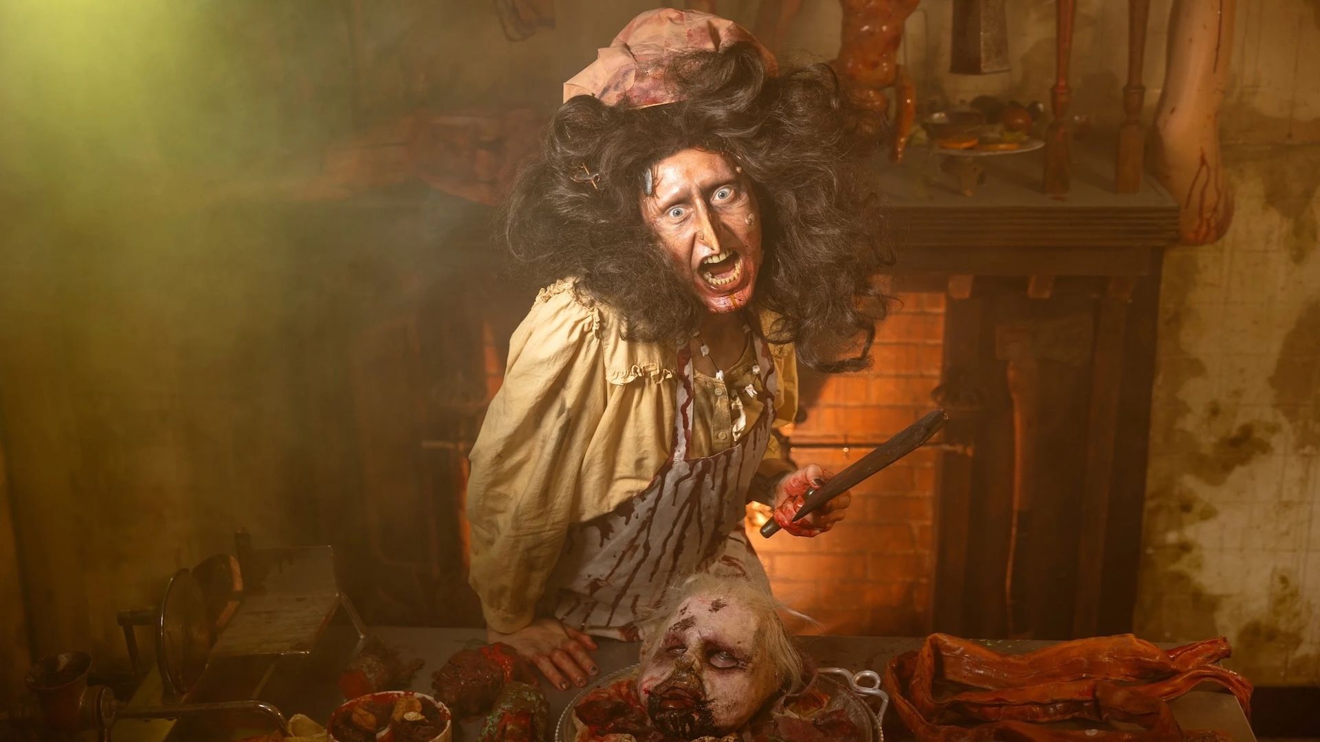 Person in blood-stained apron and old-fashioned hat with wild hair and frantic eyes in dimly lit room, holding cleaver over bloodied severed head on table with meat pieces.