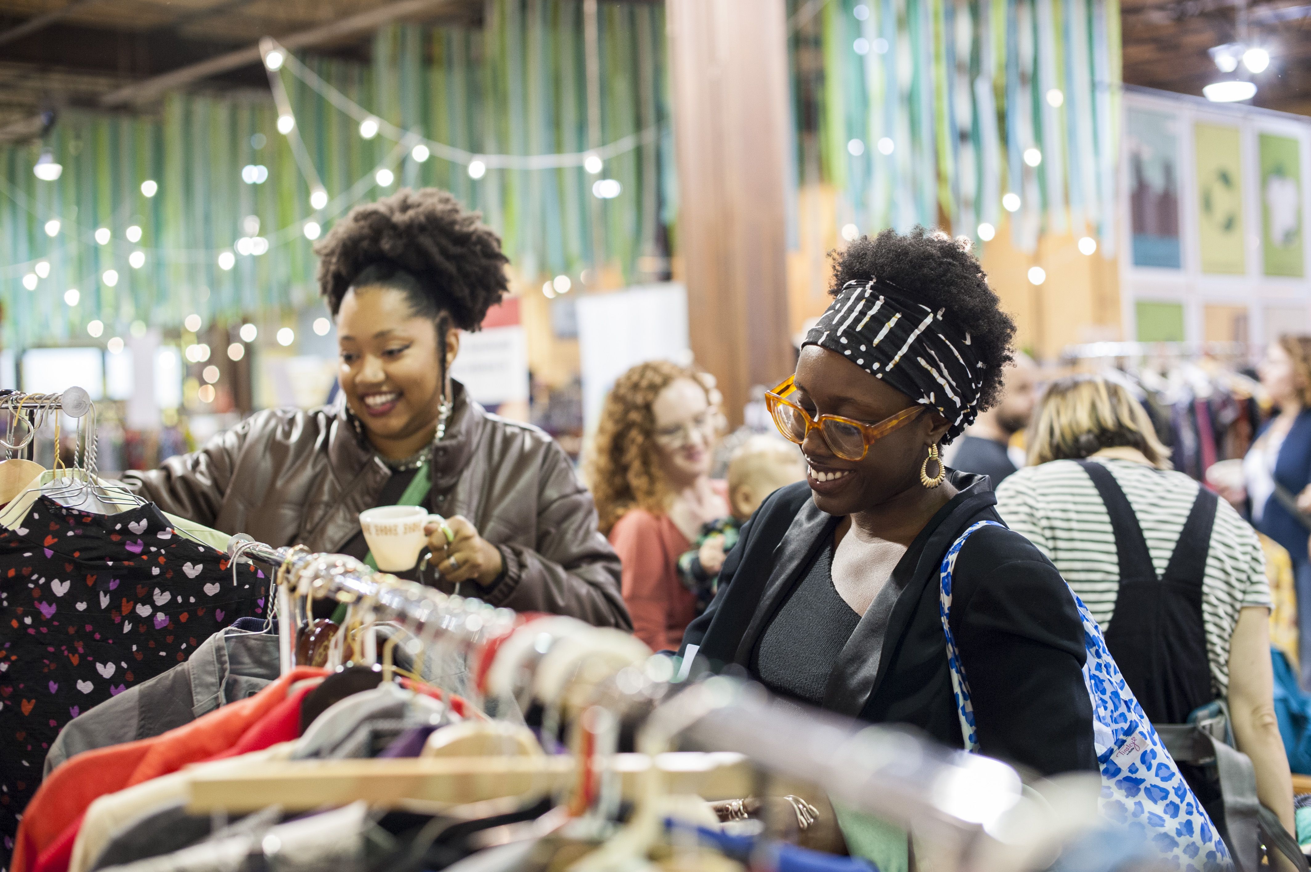 Two women combing through clothes racks, with one holding a coffee cup.