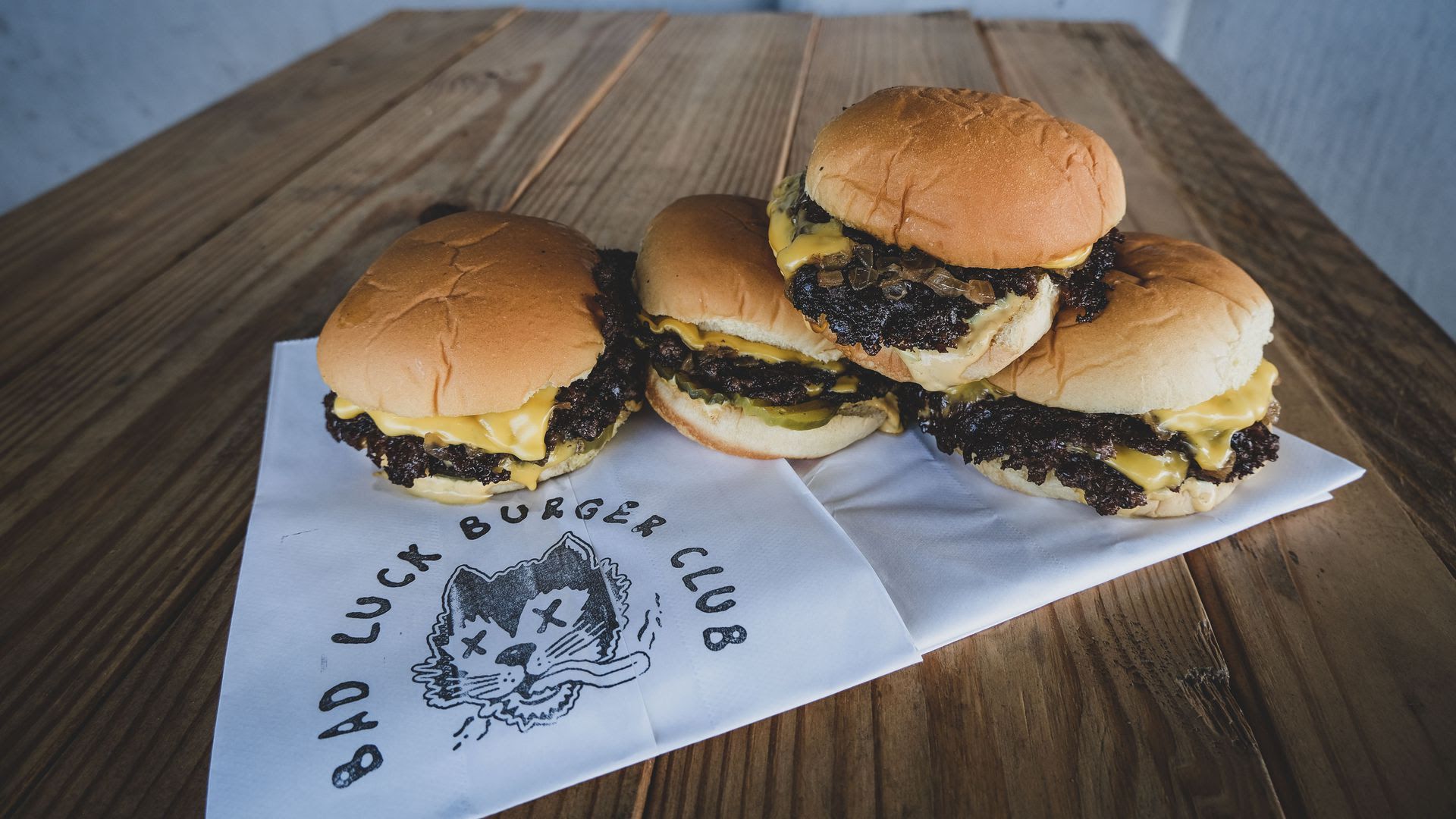 Four bad luck burgers sit on a tablecloth. 