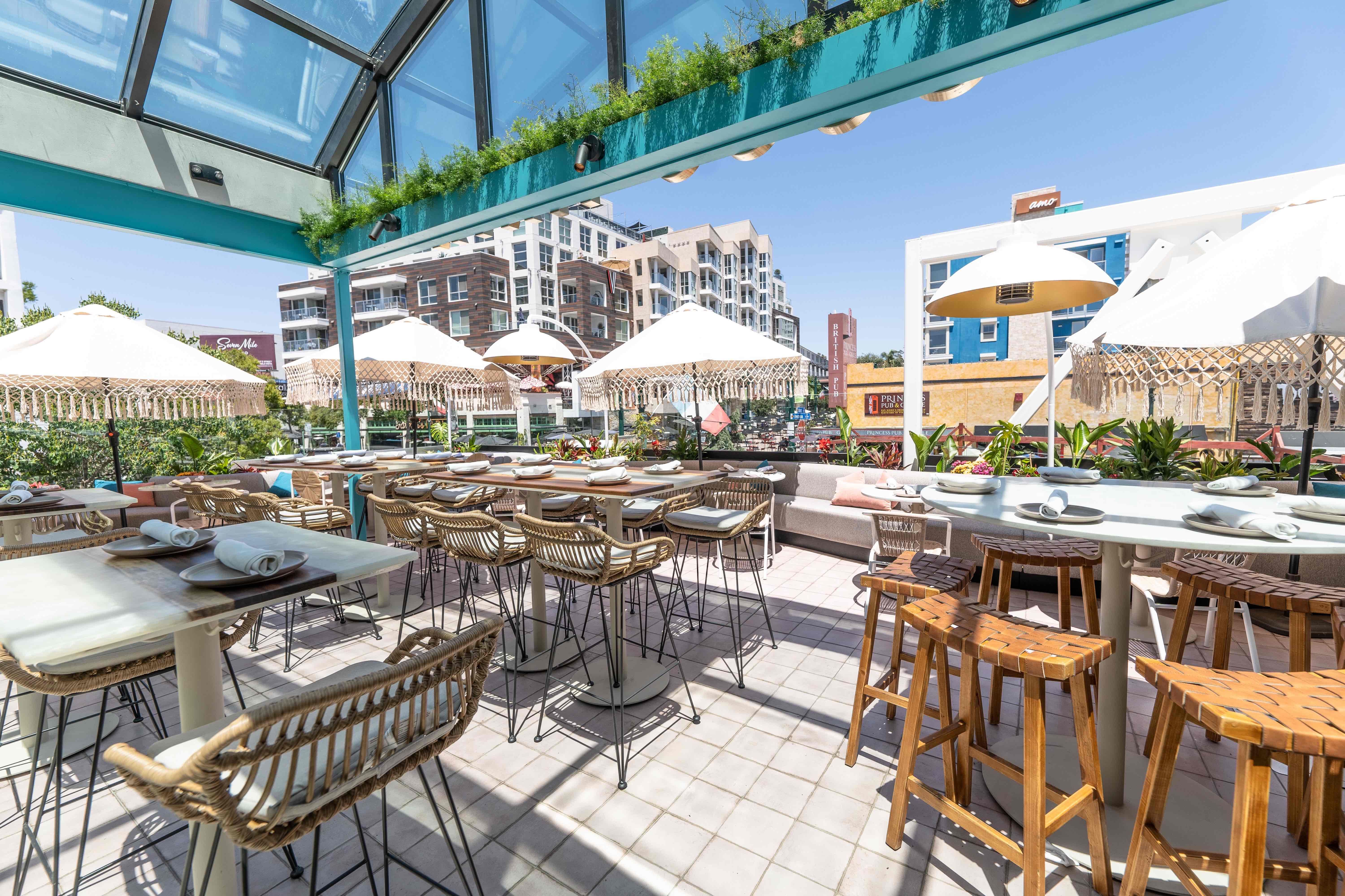 Caribbean-inspired rooftop bar with high-top tables an umbrellas on a sun day in a city.