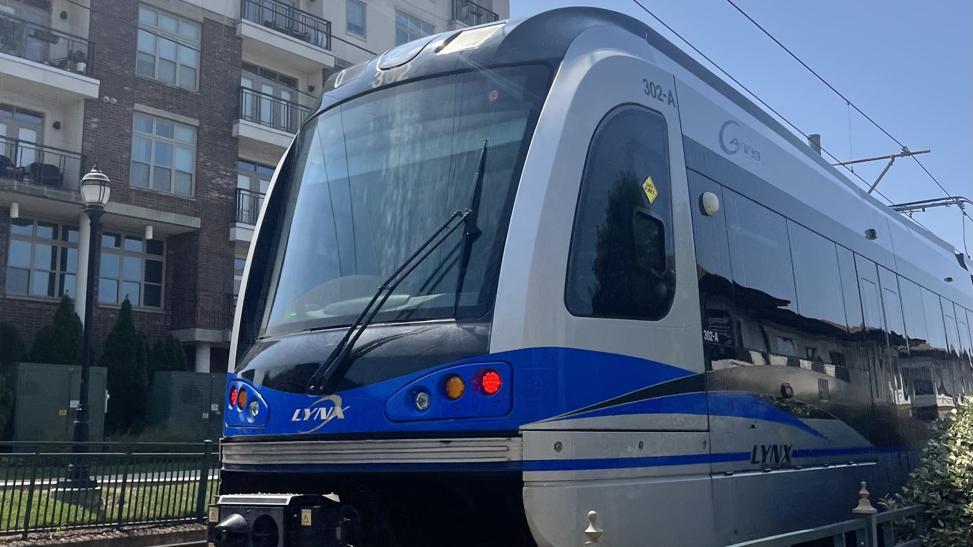 LYNX light rail train with blue and white colors on tracks next to an apartment building under a clear sky.