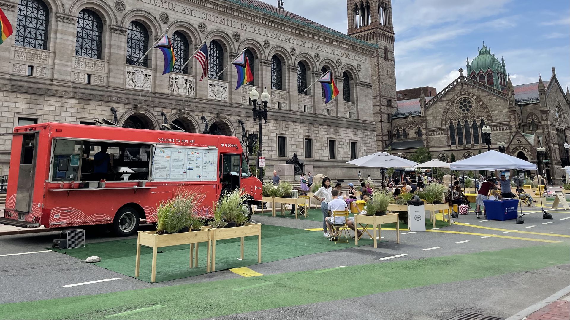 A red food truck is stationed on a closed-off section of Dartmouth Street in front of Boston Public Library. Nearby are chairs and benches.