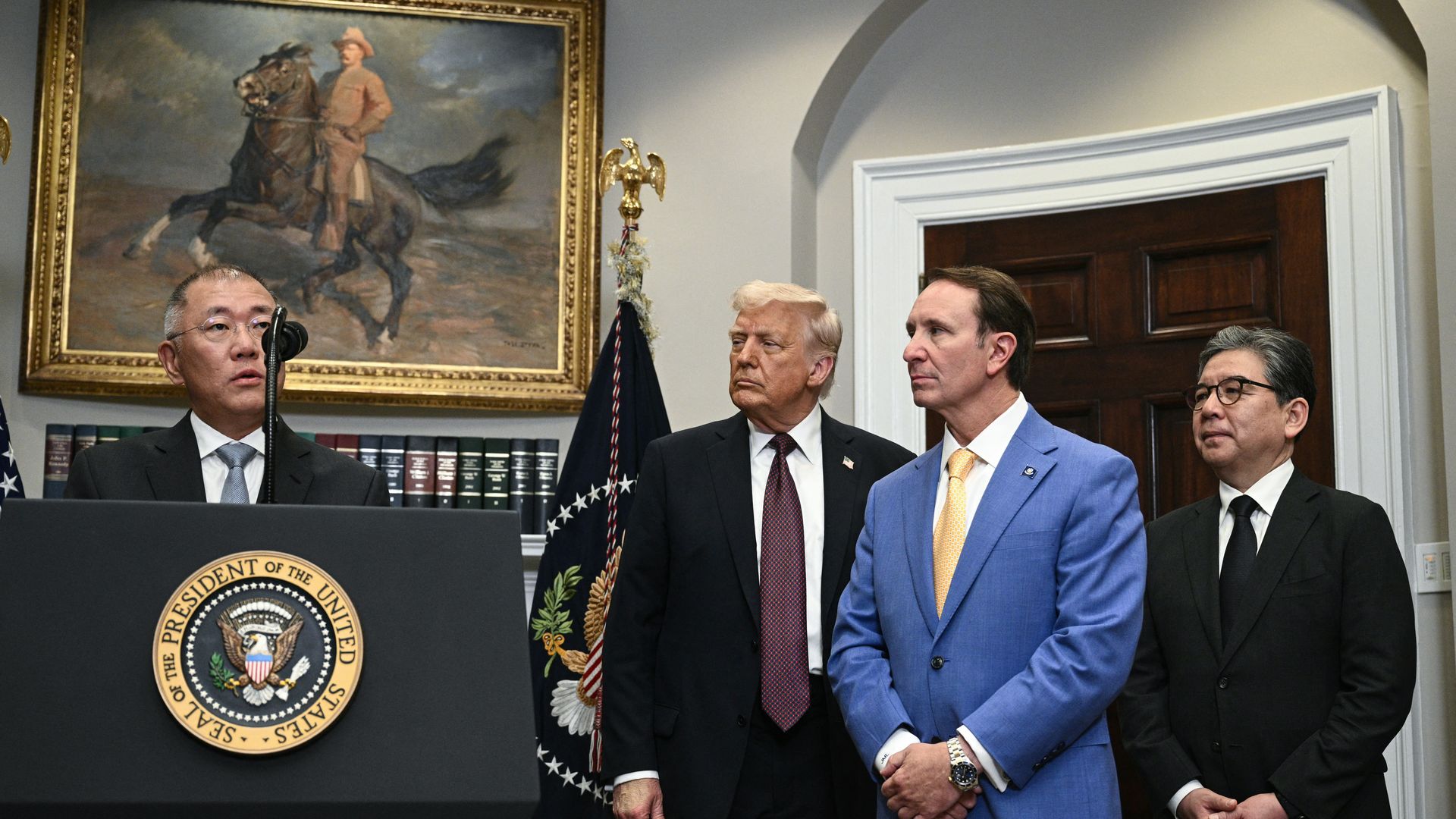 A speaks at a podium with the presidential seal while President Trump, Gov. Jeff Landry and another man stand next to him.