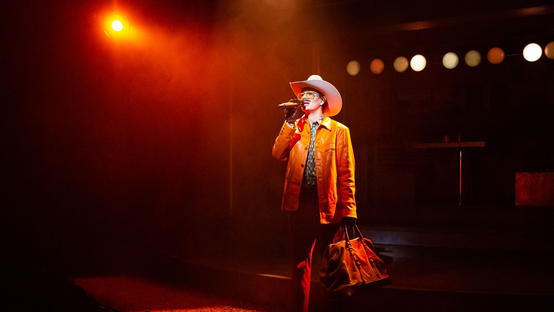 Photo of a woman on stage, wearing a cowboy hat in drag as a man. 