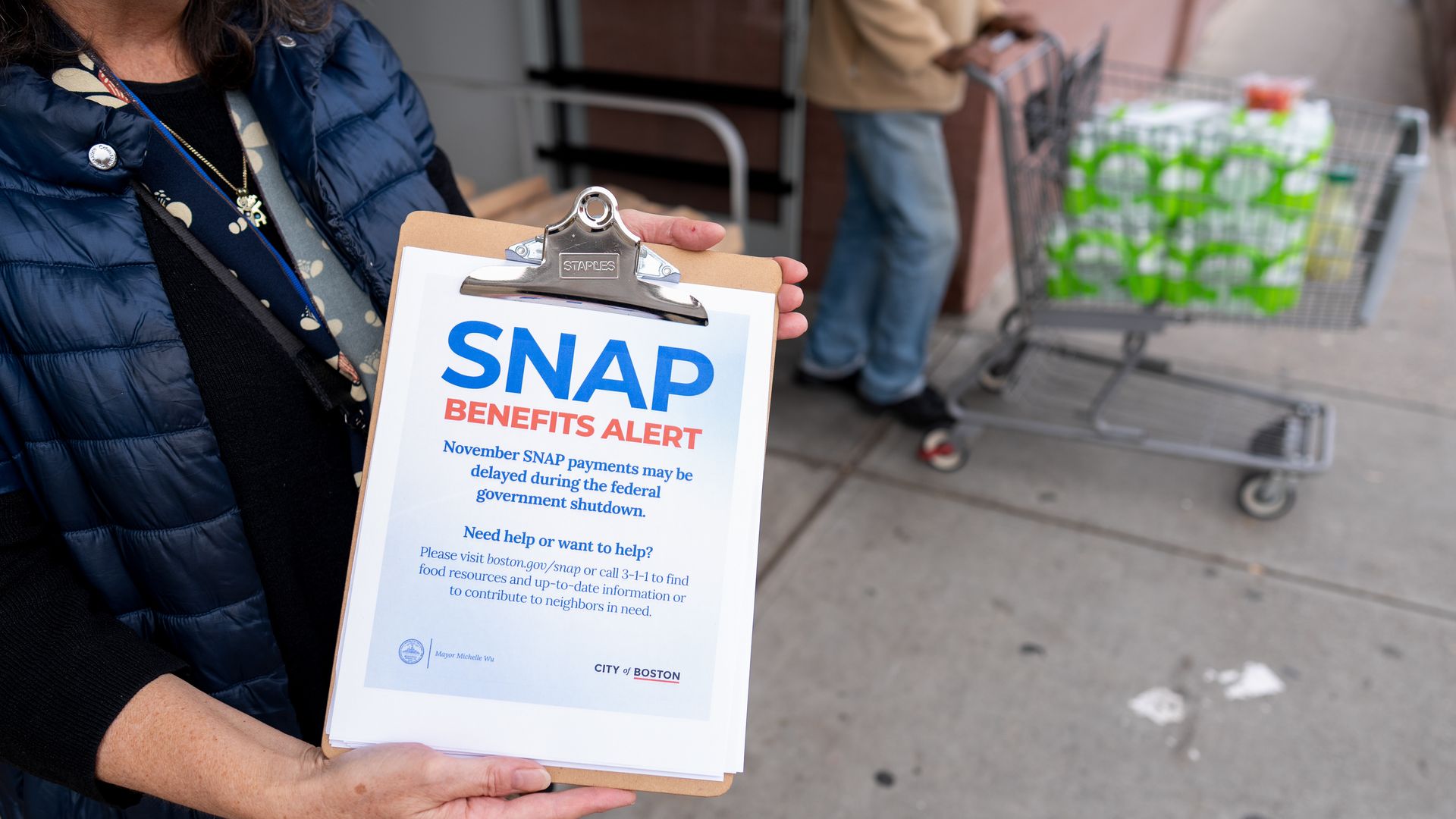 A volunteer displays information on the Supplemental Nutritional Assistance Program (SNAP) at a grocery store in Dorchester, Massachusetts, as a shopper pushes a grocery trolly. The heads of both cannot be seen.