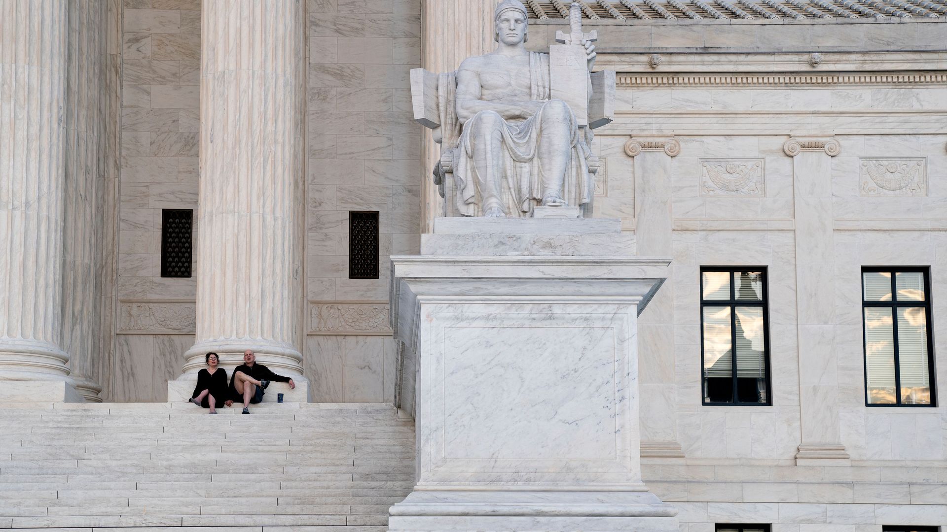 Two people are seen watching the sunset from the steps of the Supreme Court.