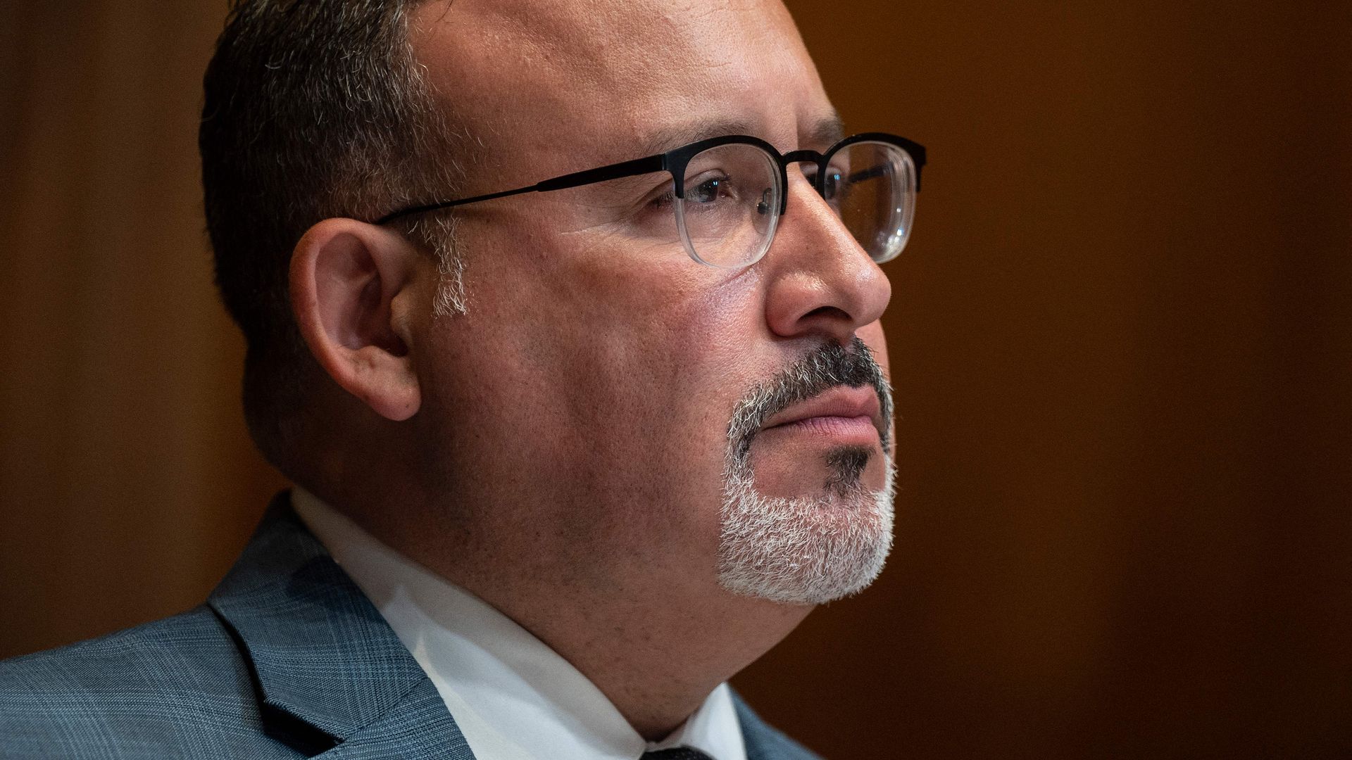 Photo of Miguel Cardona wearing an LGBTQ flag pin on his suit