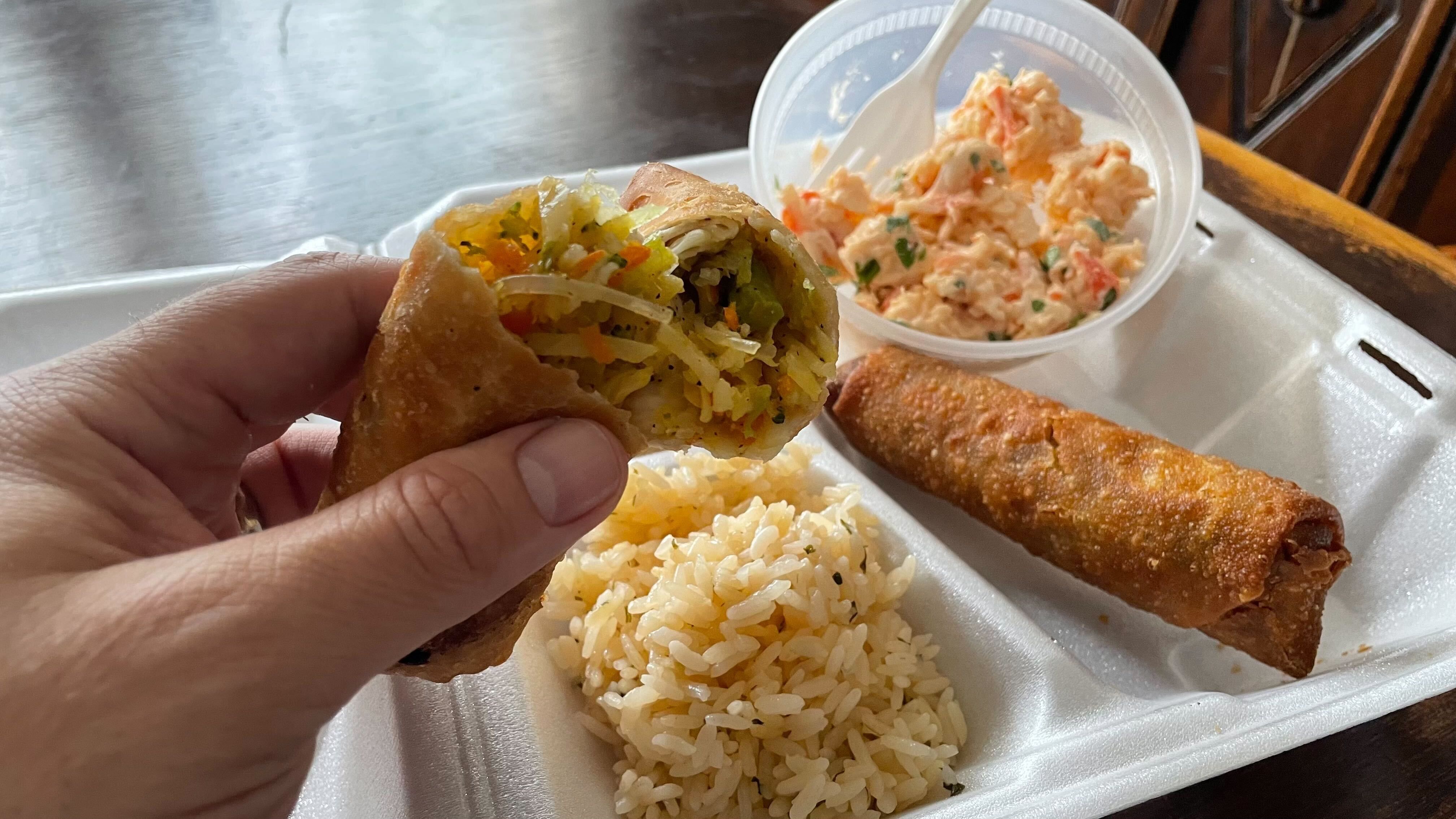 Two egg roles, a side of crab salad and rice in a Styrofoam takeaway box.